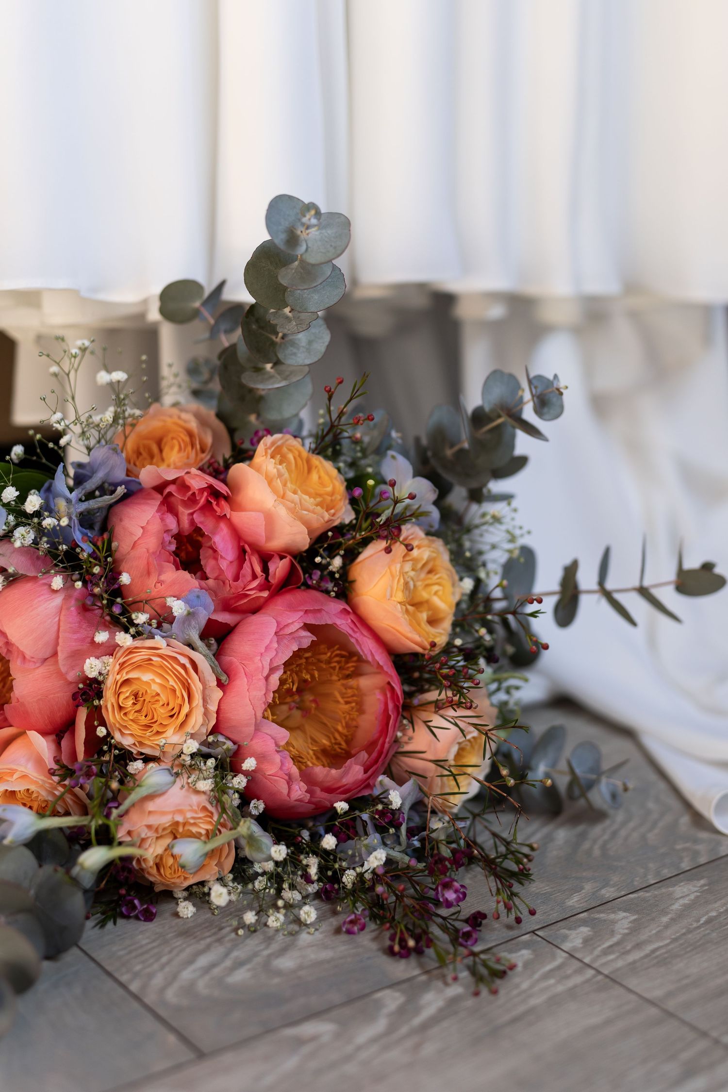 Beautiful wedding bouquet with coral peonies, peach garden roses, eucalyptus and baby's breath on gray tablecloth.