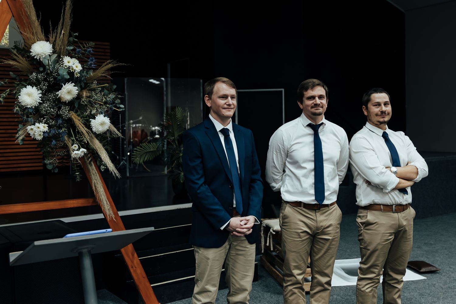 People in formal attire gathered at an evening social event with floral decorations visible.