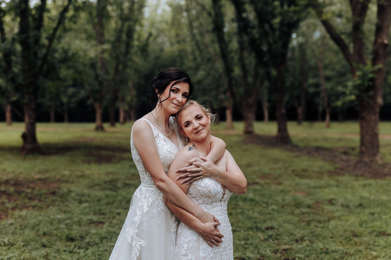 Two wedding gowns captured in an intimate moment in a forested setting.