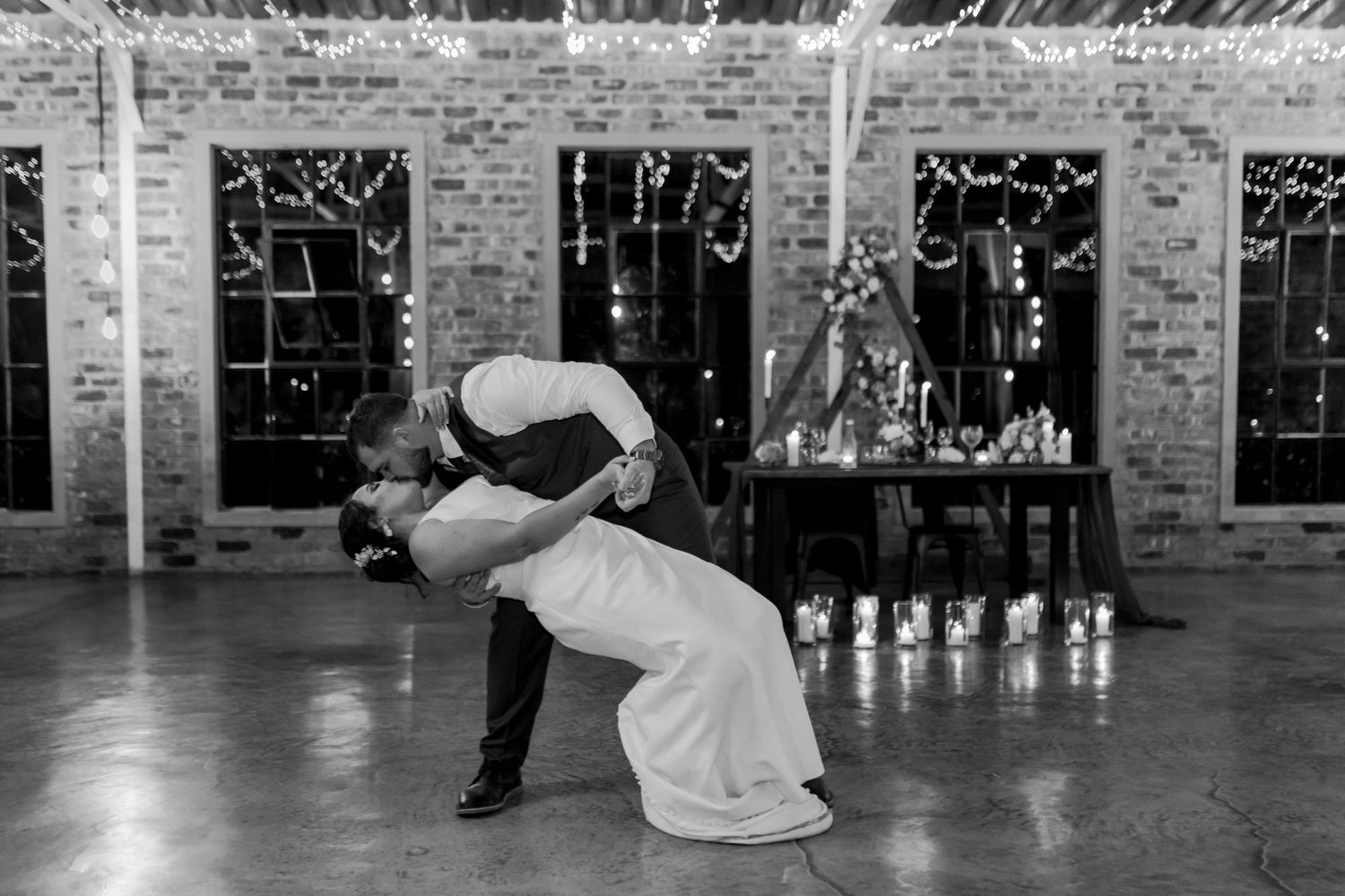 A dramatic black and white photo of a wedding dance dip in front of exposed brick walls.