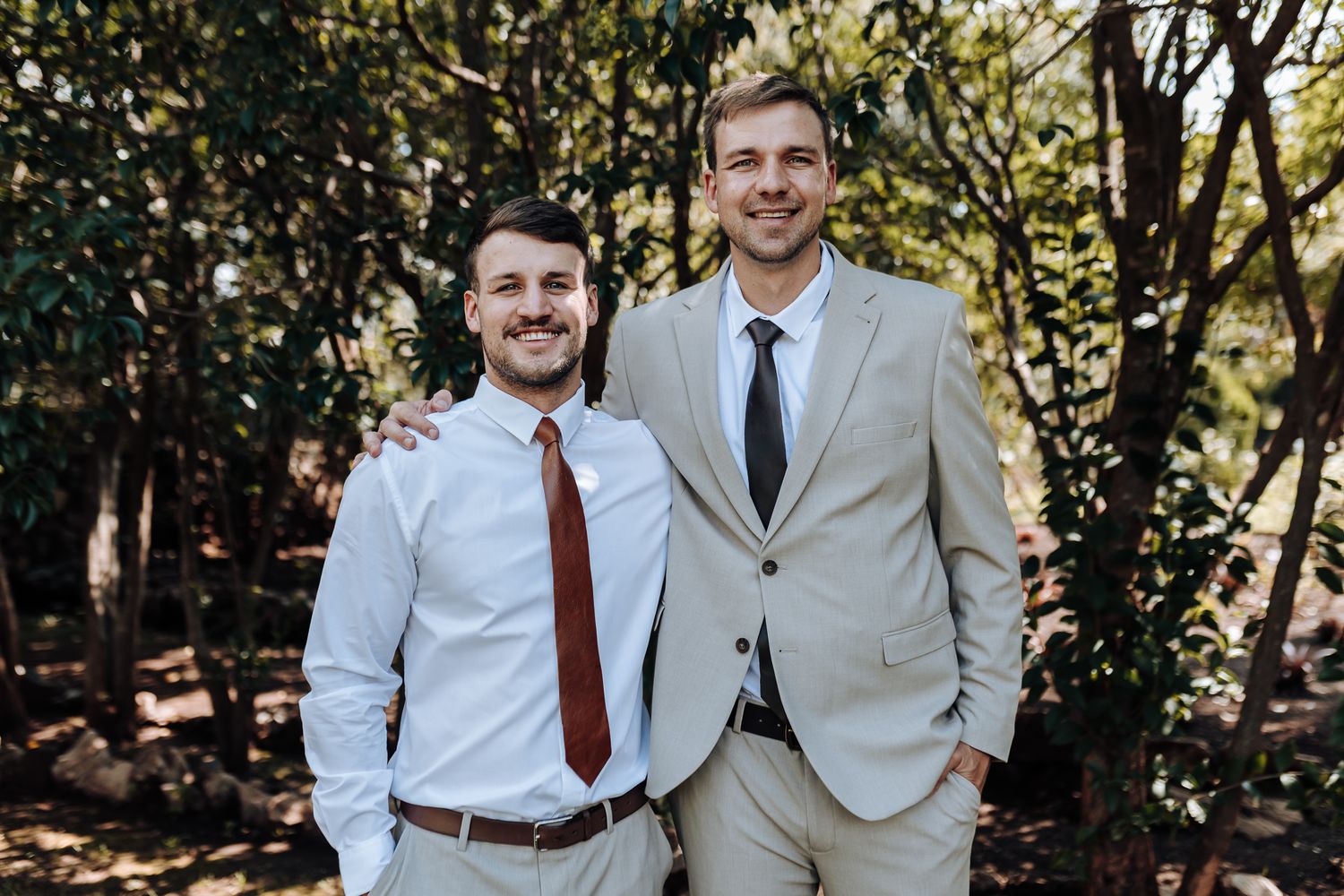 Two men in light colored suits smiling together outdoors.