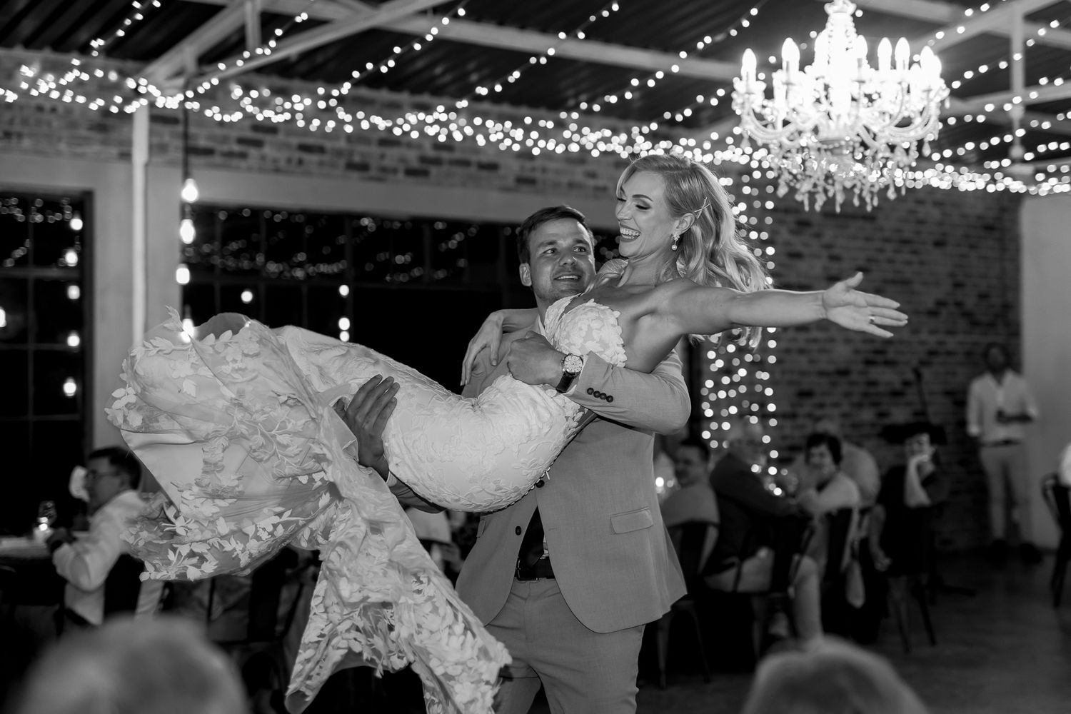 Black and white photo of romantic wedding dance moment under twinkling lights.