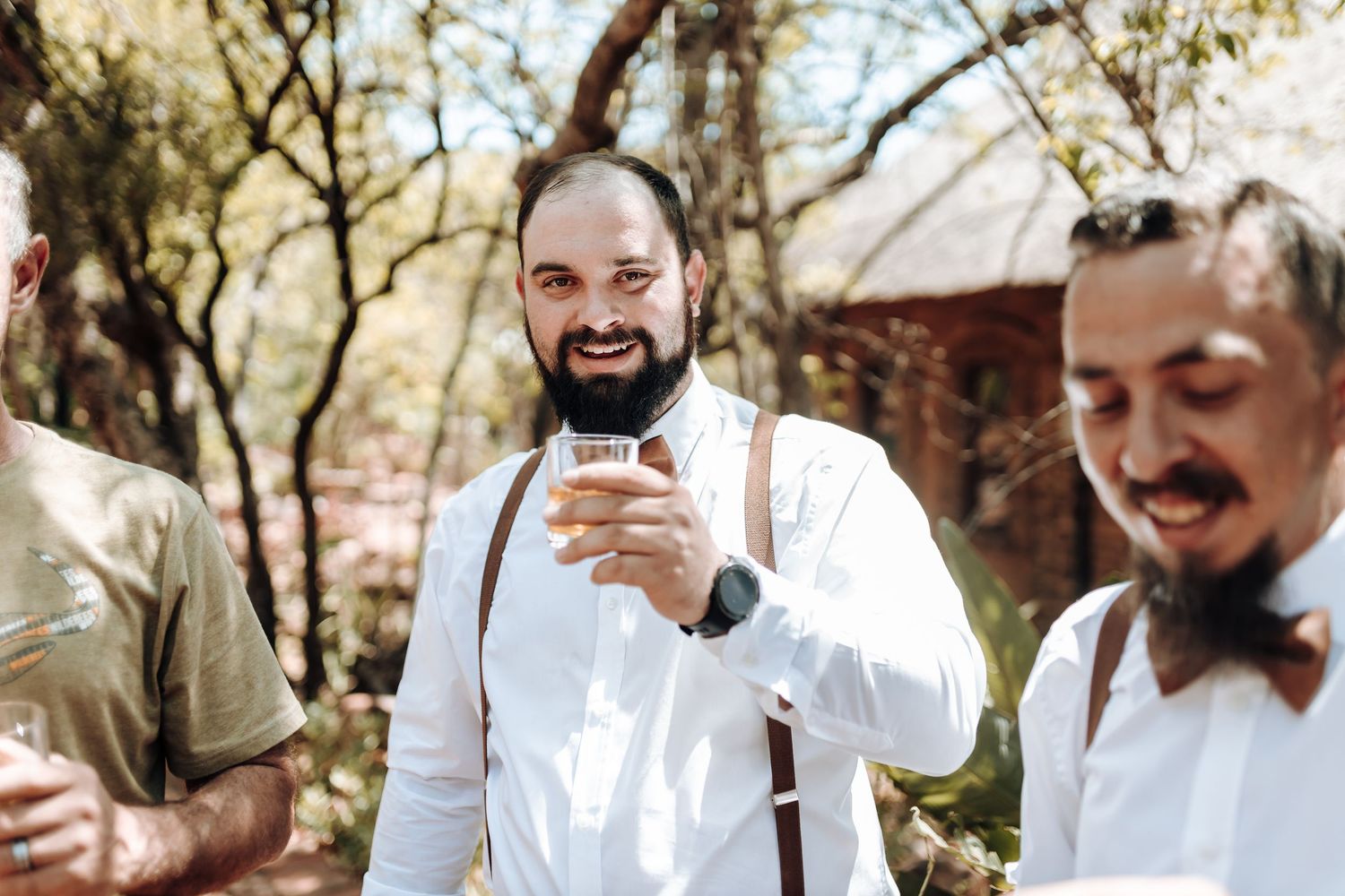 A group in formal attire with suspenders enjoying drinks in an outdoor setting.