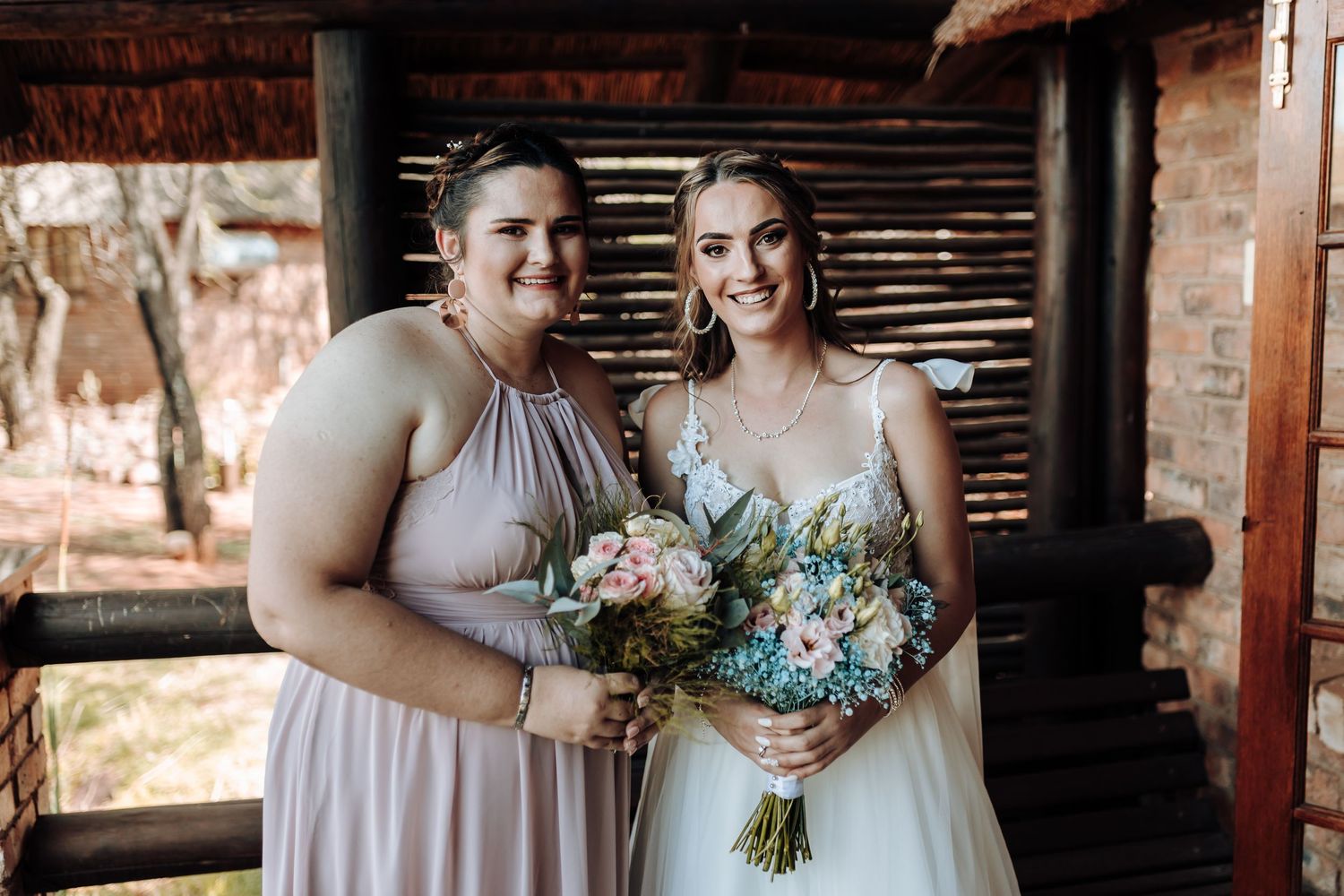 Candid wedding photo of bridesmaid and bride posing under rustic wooden shelter.