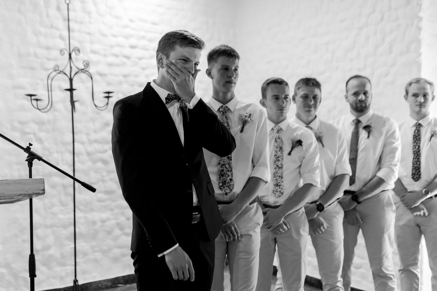 Wedding party members stand at altar in formal attire during emotional ceremony moment.