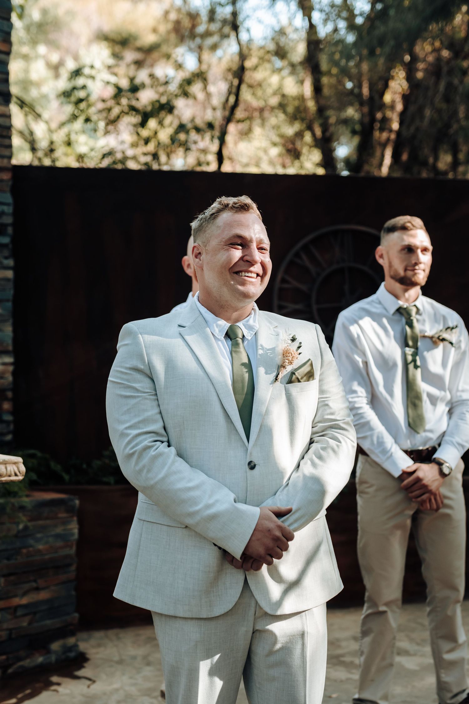 A joyful moment captured during an outdoor wedding ceremony with groomsmen in light suits.