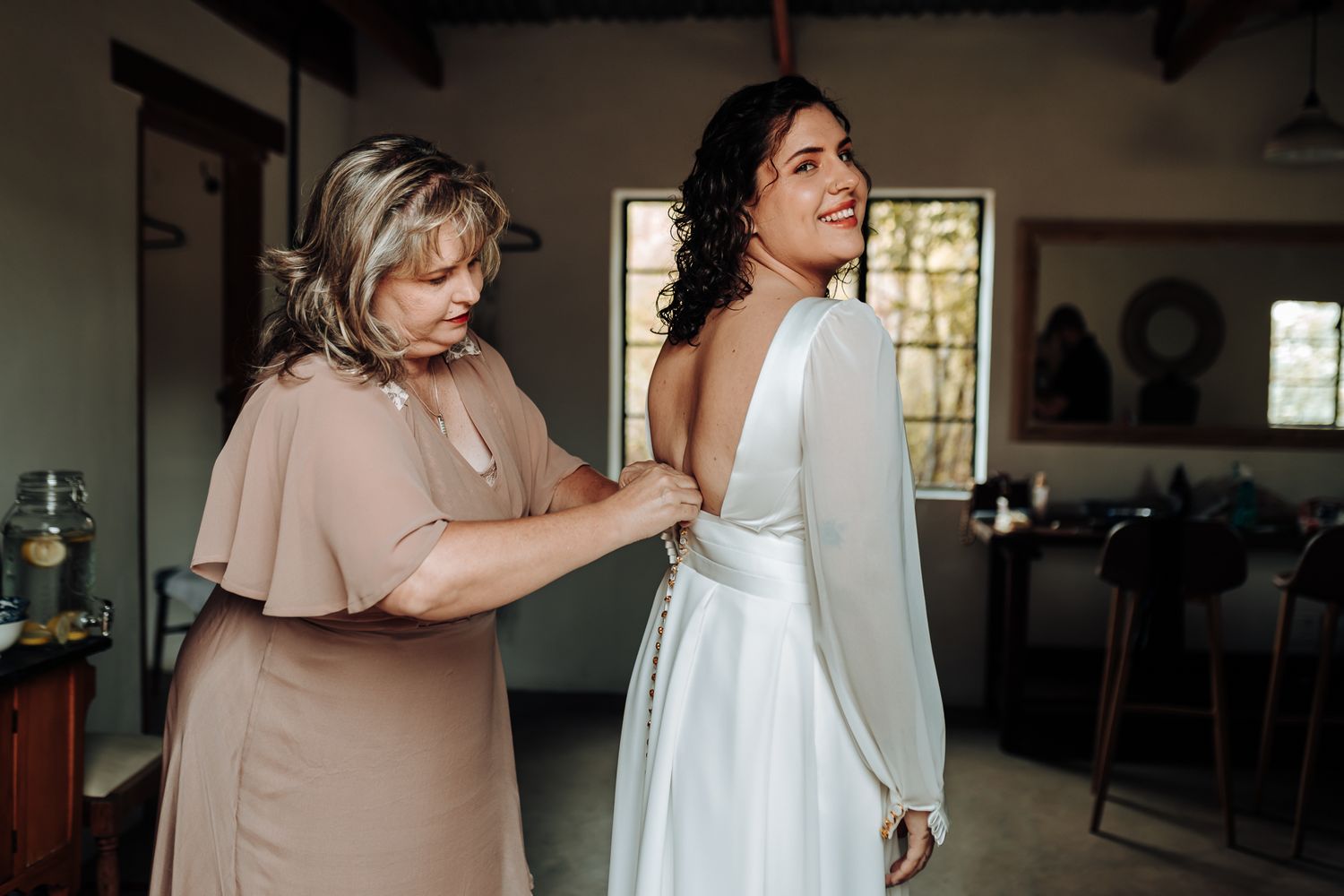 Wedding dress preparation moment captured in indoor rustic setting.