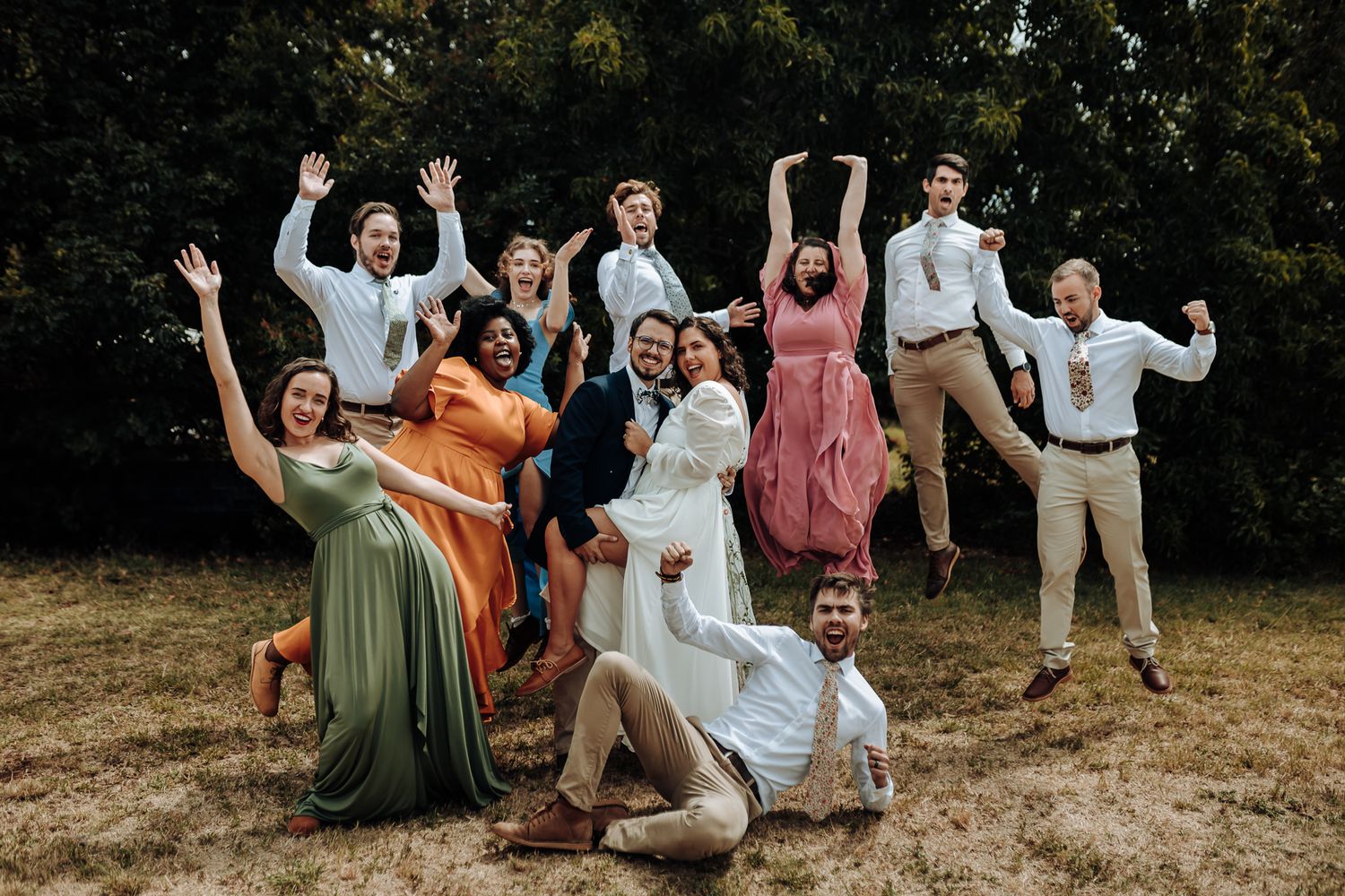 Wedding party strikes playful jumping poses for fun group photo outdoors.