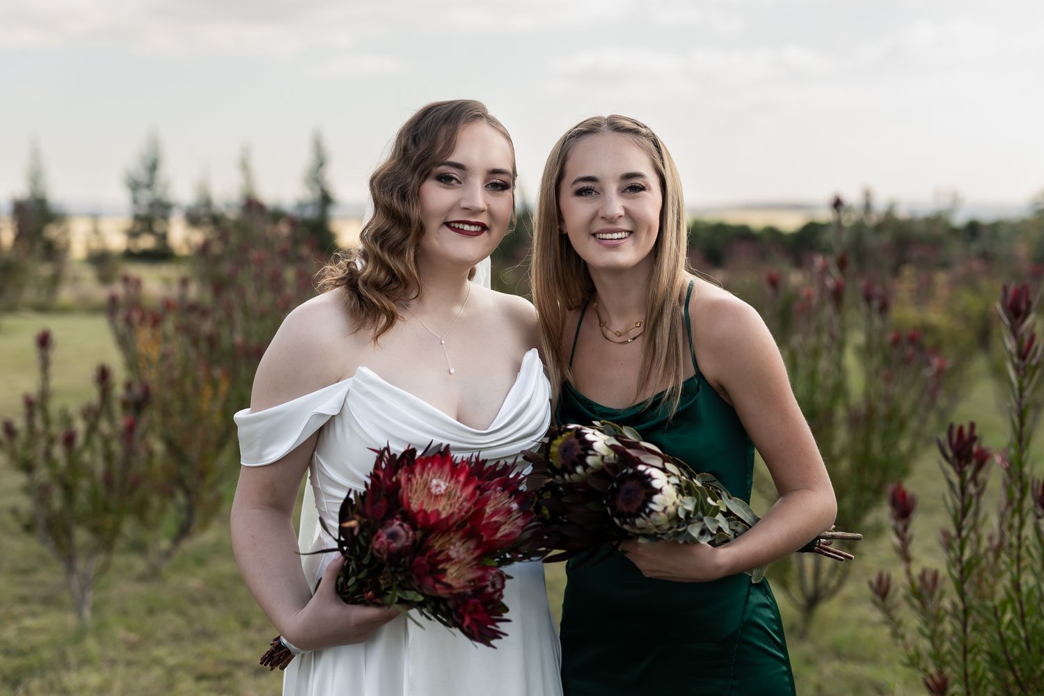 Bridal party holding bouquets pose together in outdoor garden setting.