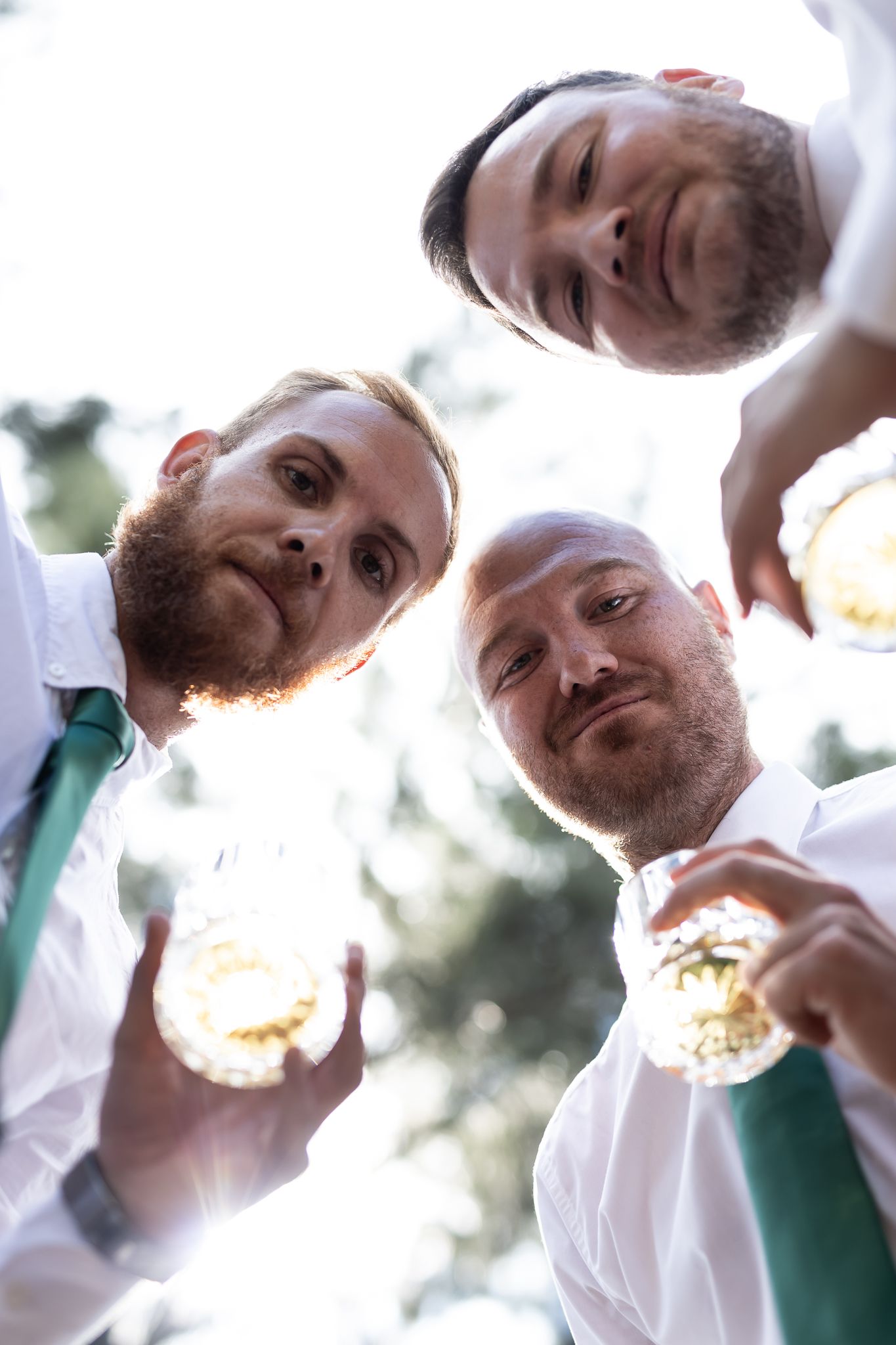 Three friends enjoying drinks together captured from below against a bright sky.
