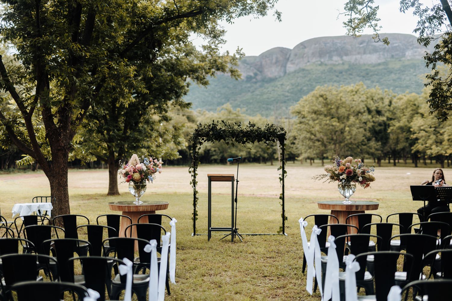 An outdoor wedding ceremony setup with black chairs and mountain backdrop.