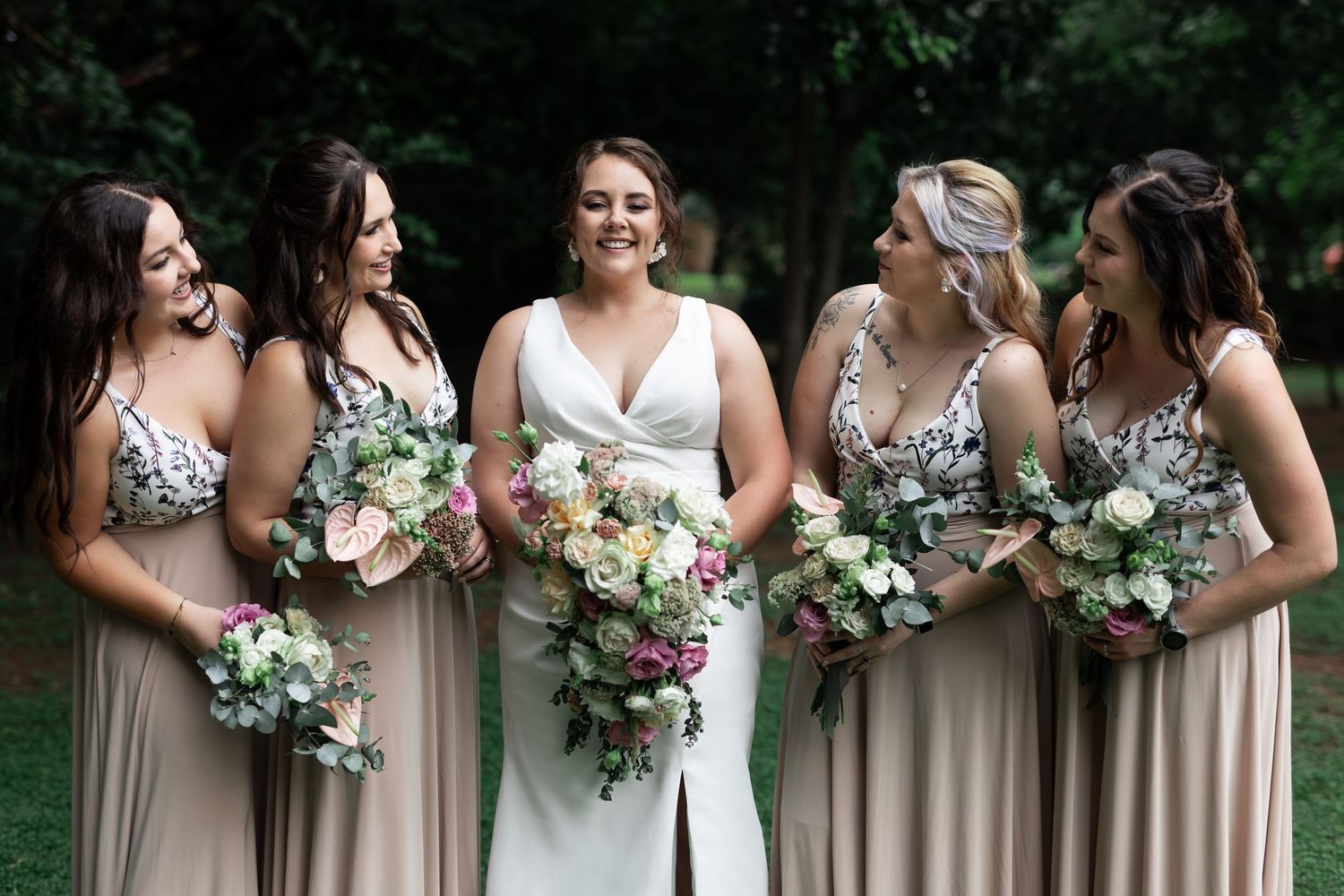 Wedding party with bridesmaids in floral dresses holding bouquets outdoors.