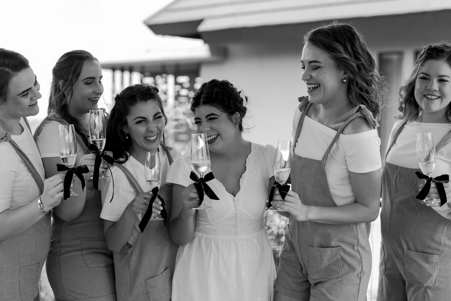 Black and white photo of wedding party laughing together on outdoor porch.