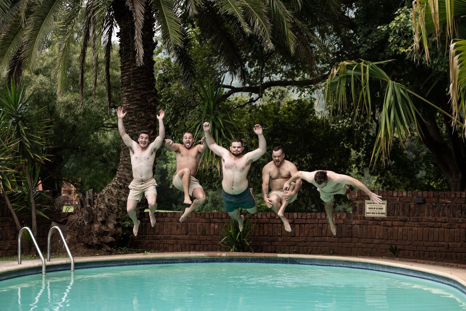 Group jumping into a pool surrounded by tropical palm trees on a sunny day.