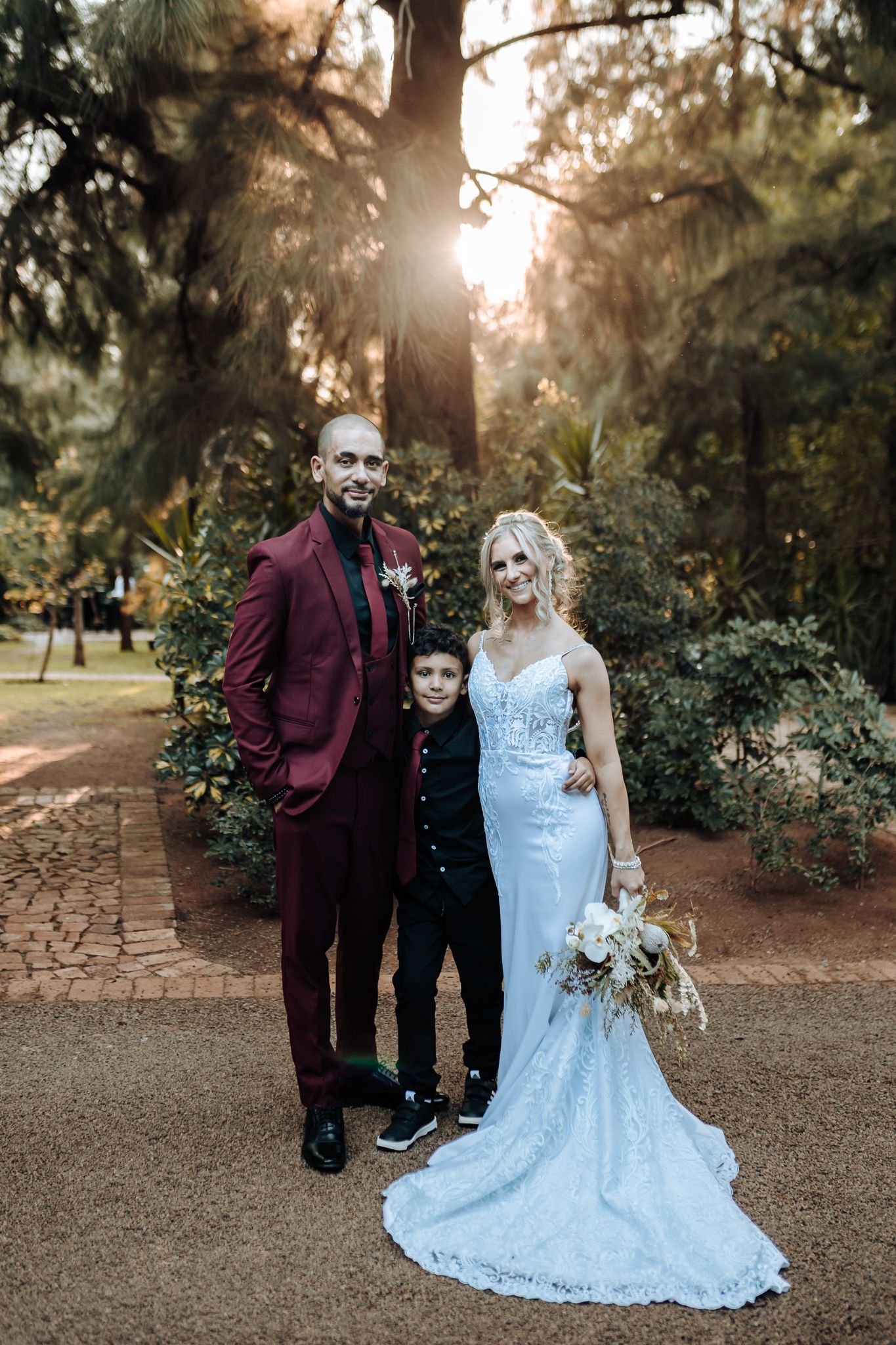 Family poses for formal wedding portrait on garden path at sunset.