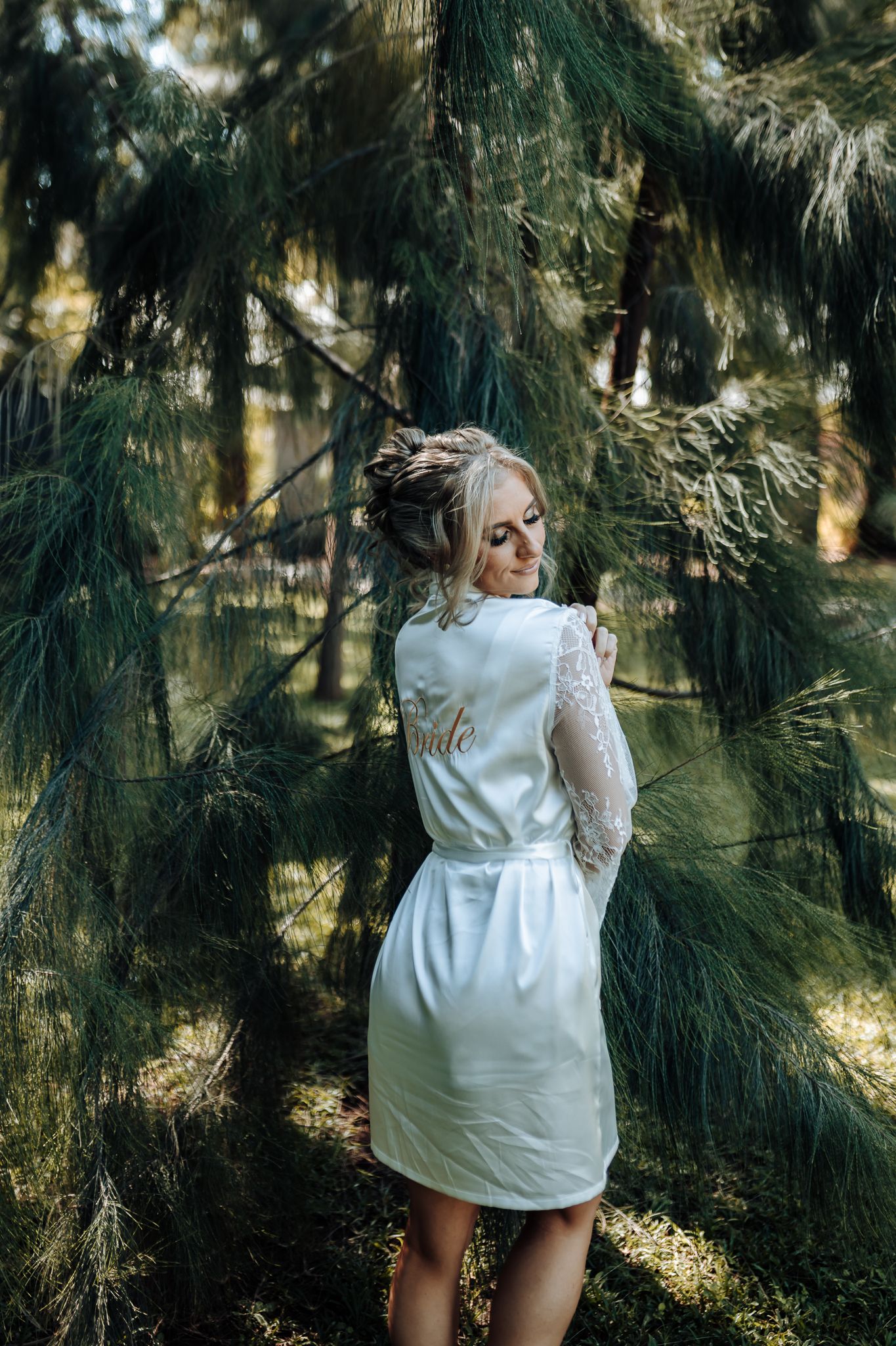 Outdoor portrait in a pine forest wearing a white satin robe.