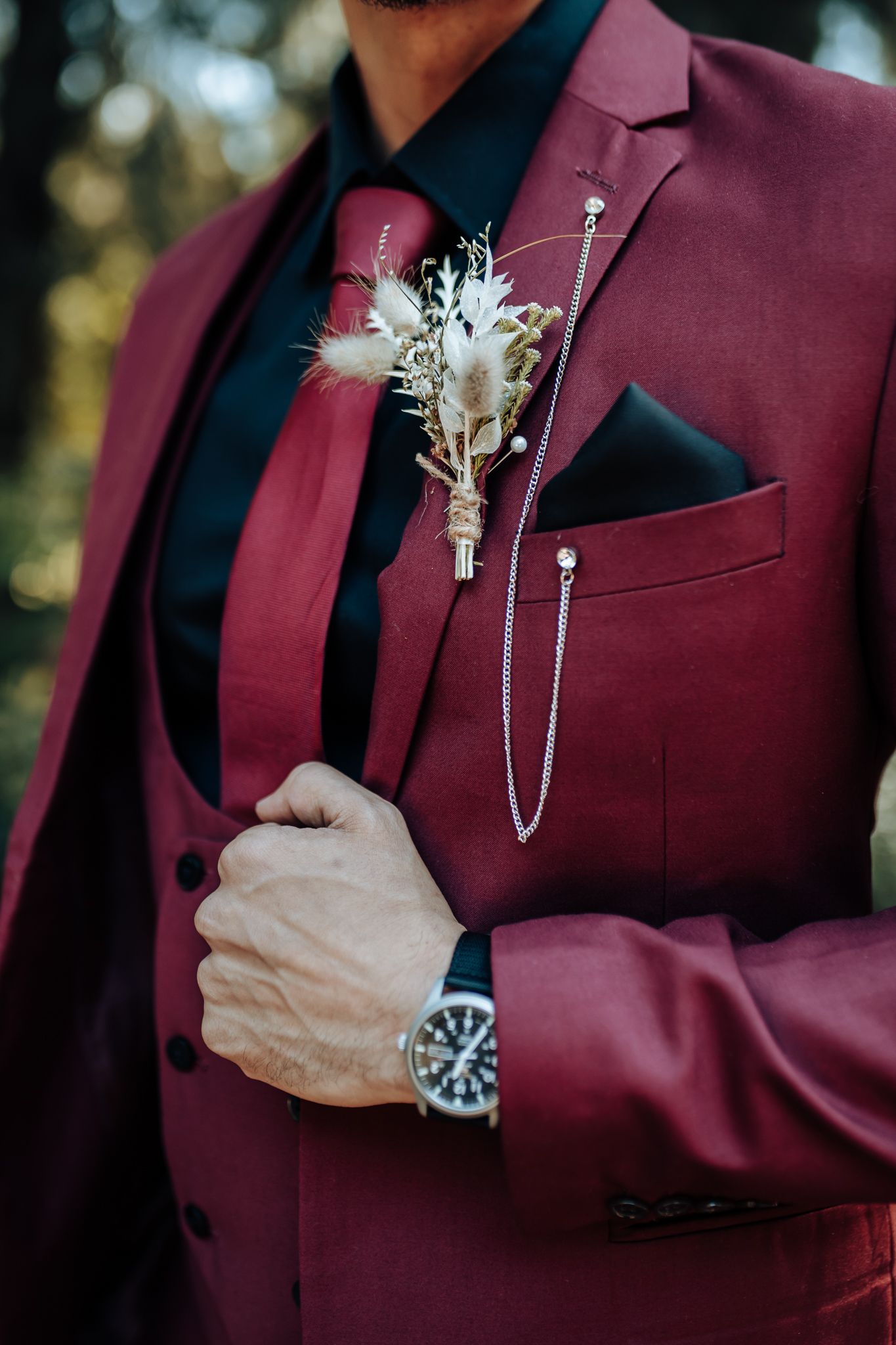 Close-up of burgundy suit jacket with white boutonniere and pocket square details.