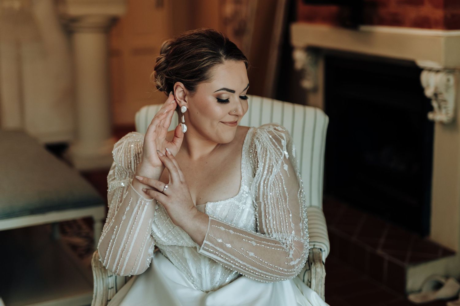 Elegant bridal portrait showing a white wedding gown with sheer beaded long sleeves and statement earrings.
