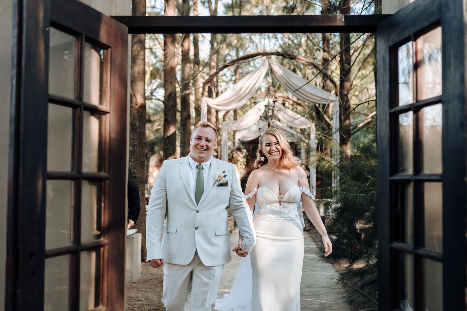 A couple exits through large wooden doors after their wedding ceremony in a wooded setting.