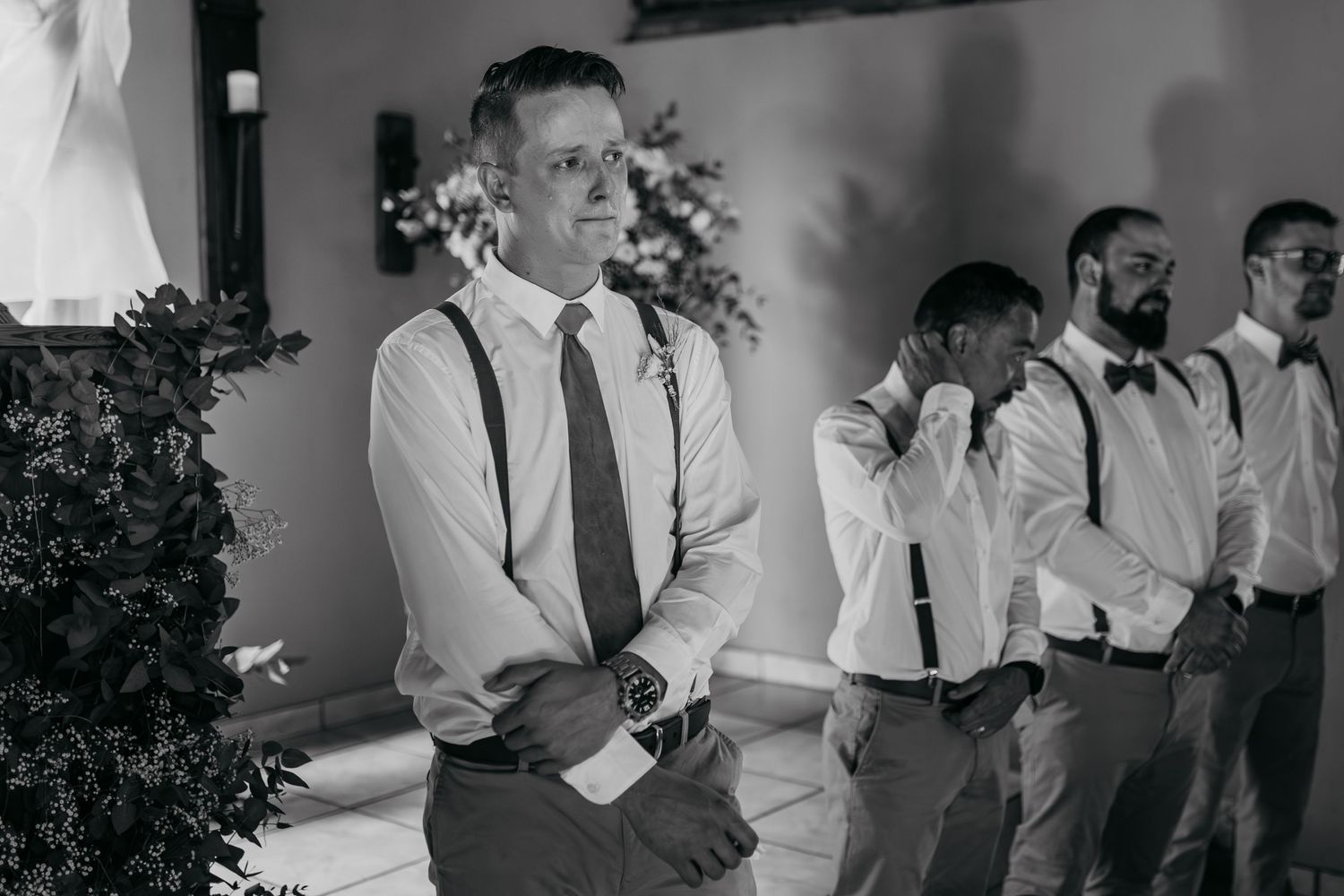 Black and white photo of groomsmen standing in formation at a rustic wedding venue.