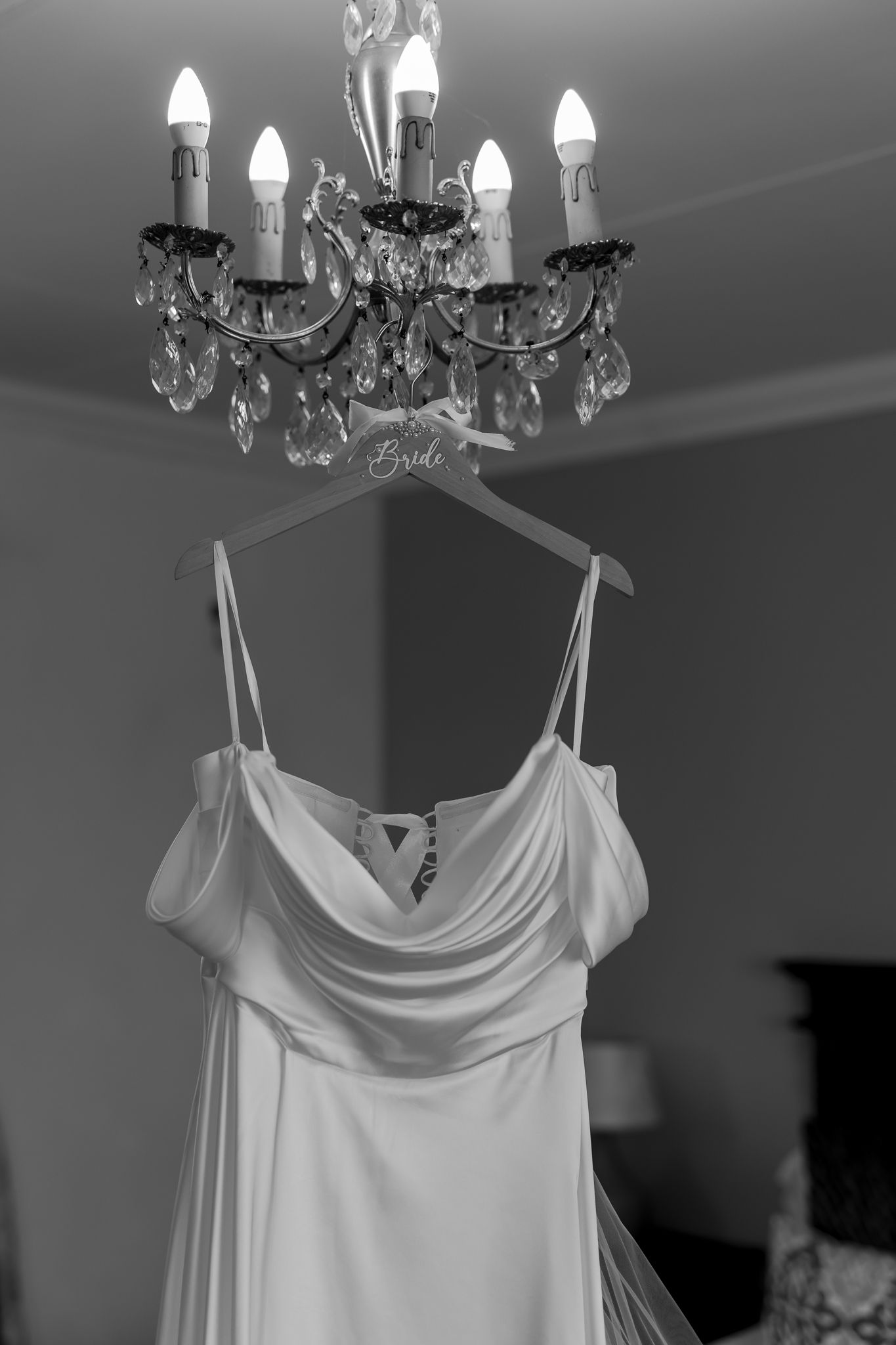Crystal chandelier hangs above an elegant white wedding dress on display.
