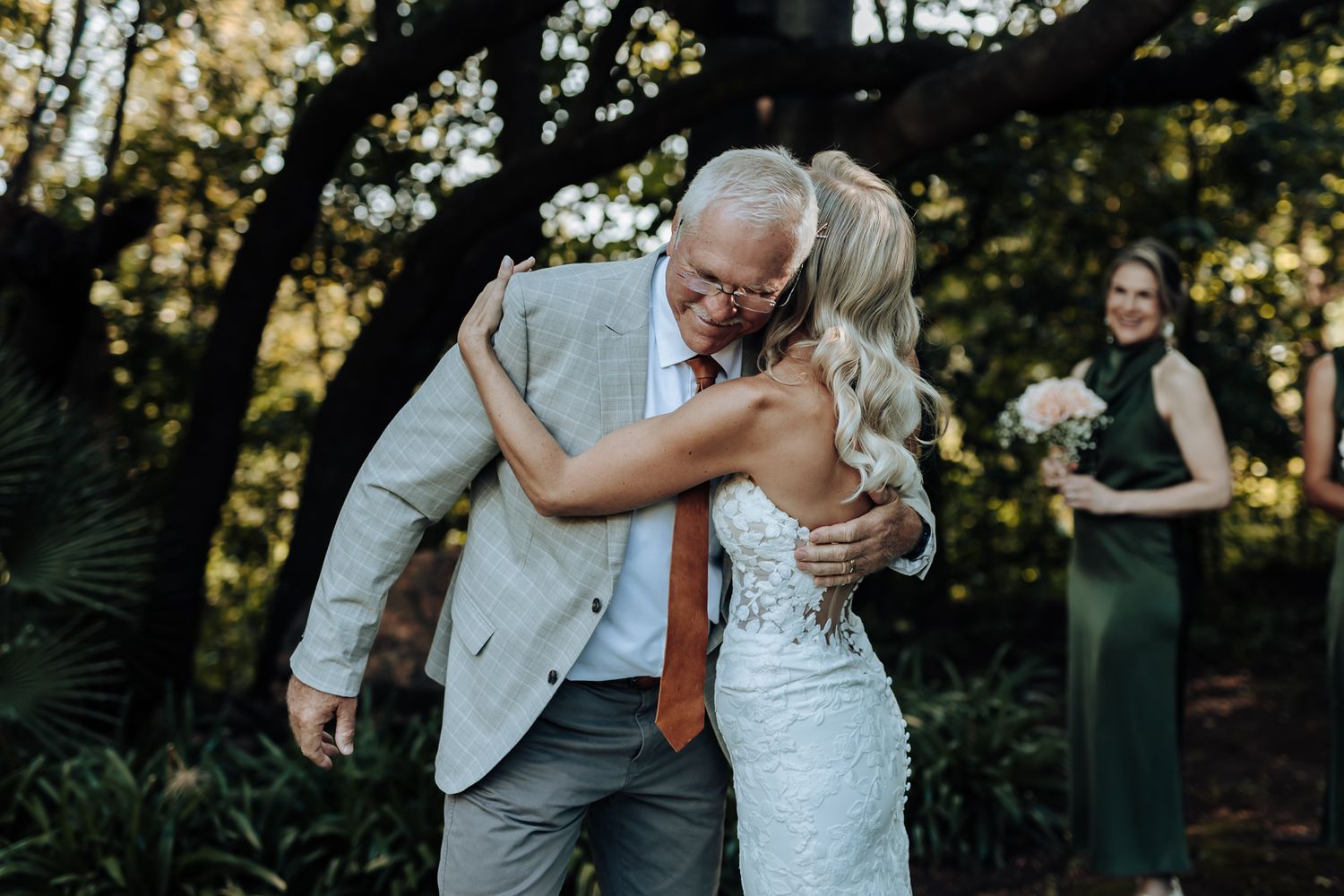 Emotional embrace during outdoor wedding ceremony with bridesmaids in green dresses watching.