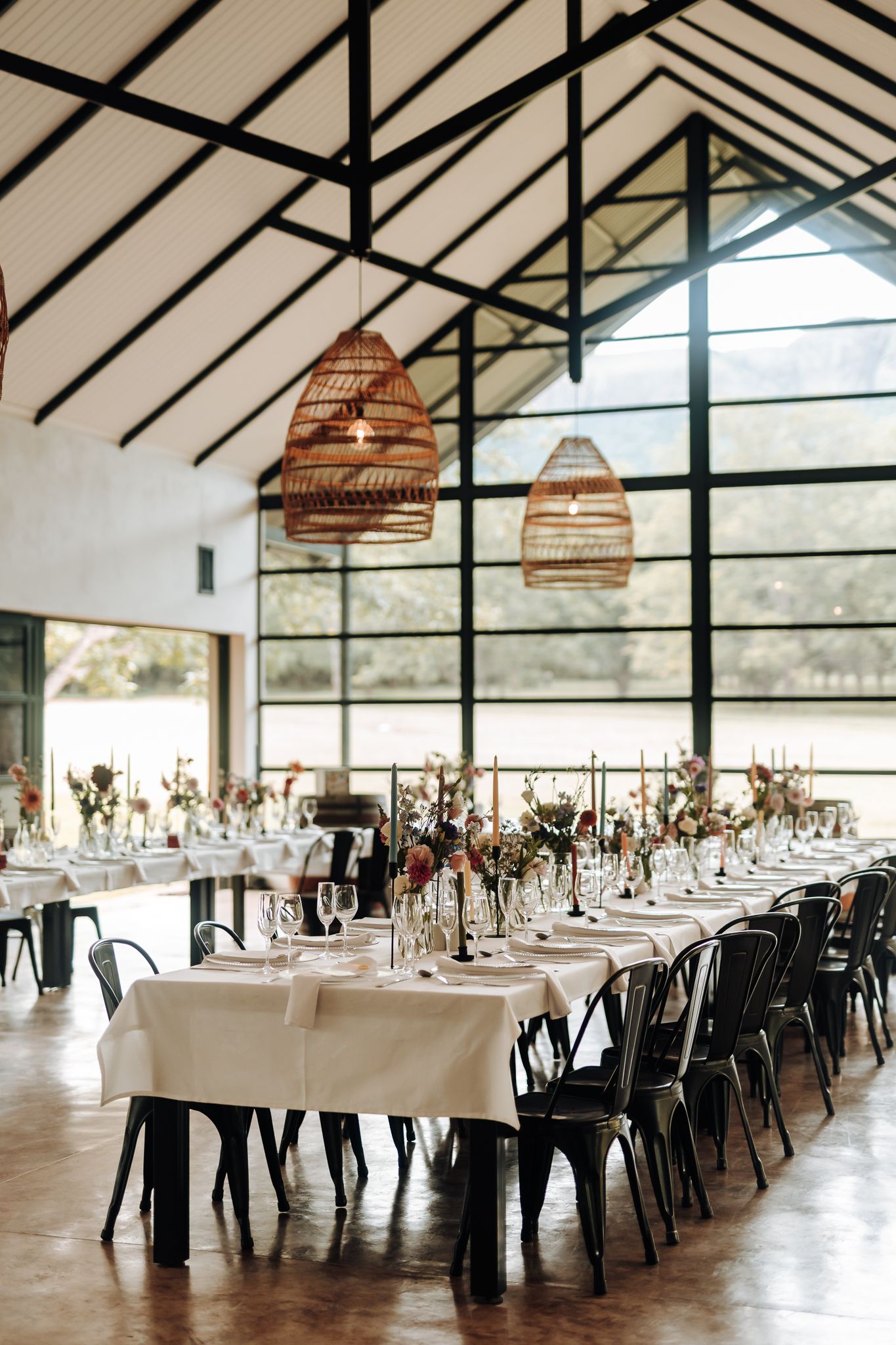 Modern wedding reception space with long tables and woven basket pendant lights creating a warm atmosphere.
