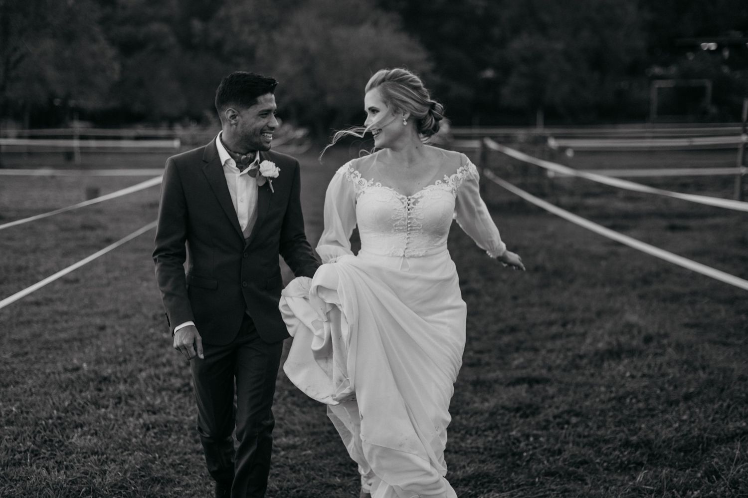 Black and white wedding photo of couple walking together on manicured grounds.