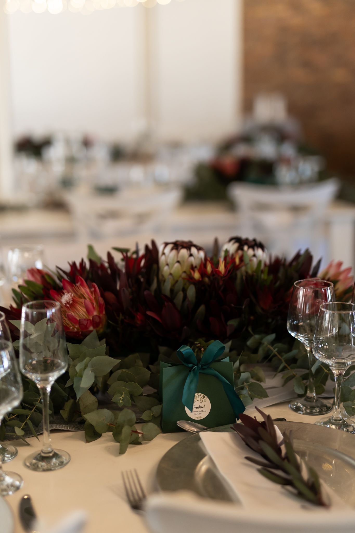 Elegant table setting with protea flowers and eucalyptus centerpiece at wedding reception.