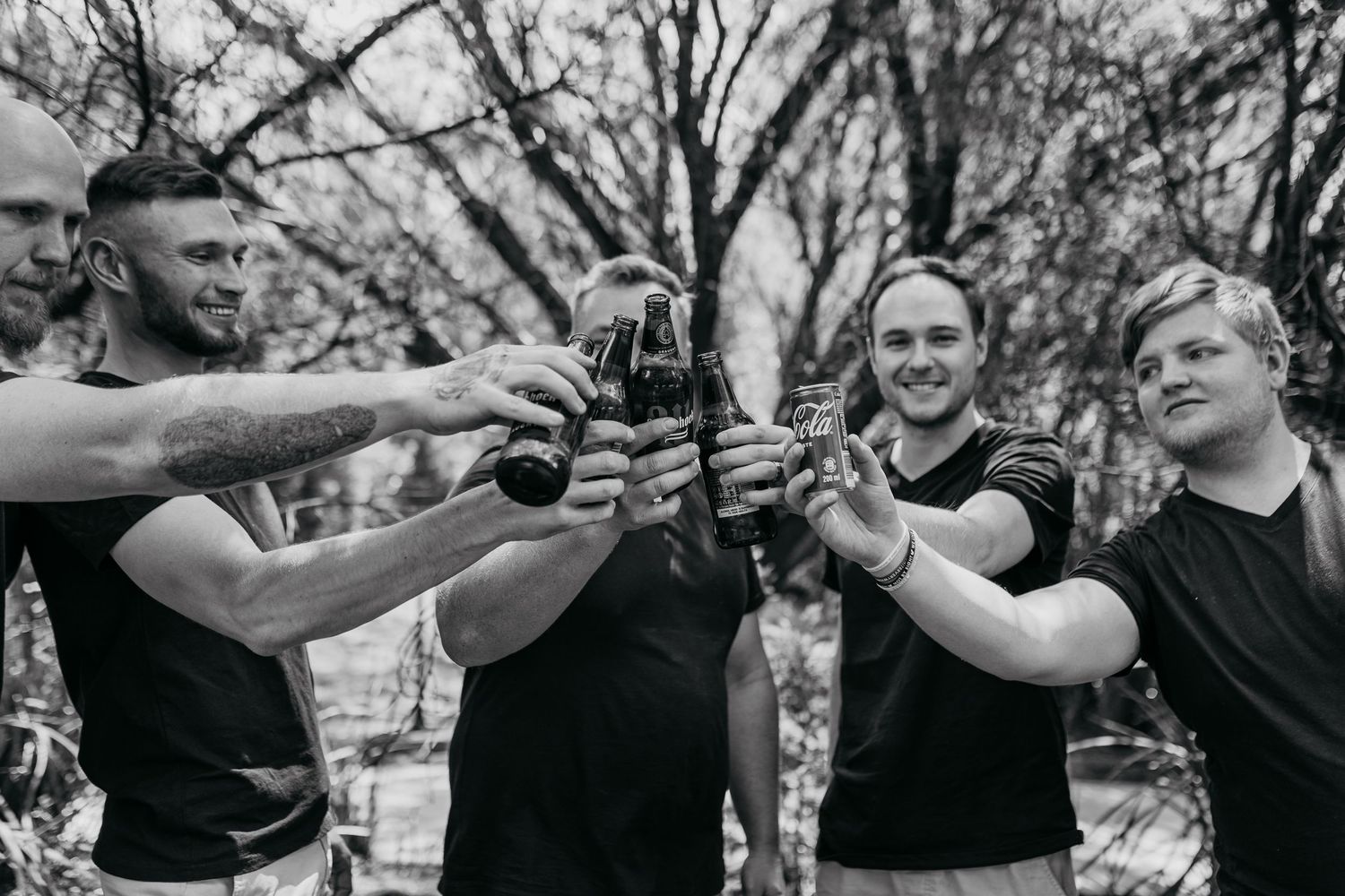 Friends in black shirts toasting and clinking beer bottles together outdoors.