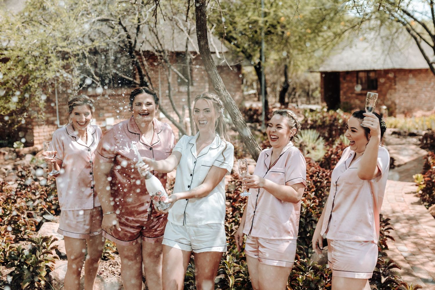 Group celebrating with confetti while wearing coordinated satin sleepwear outdoors.