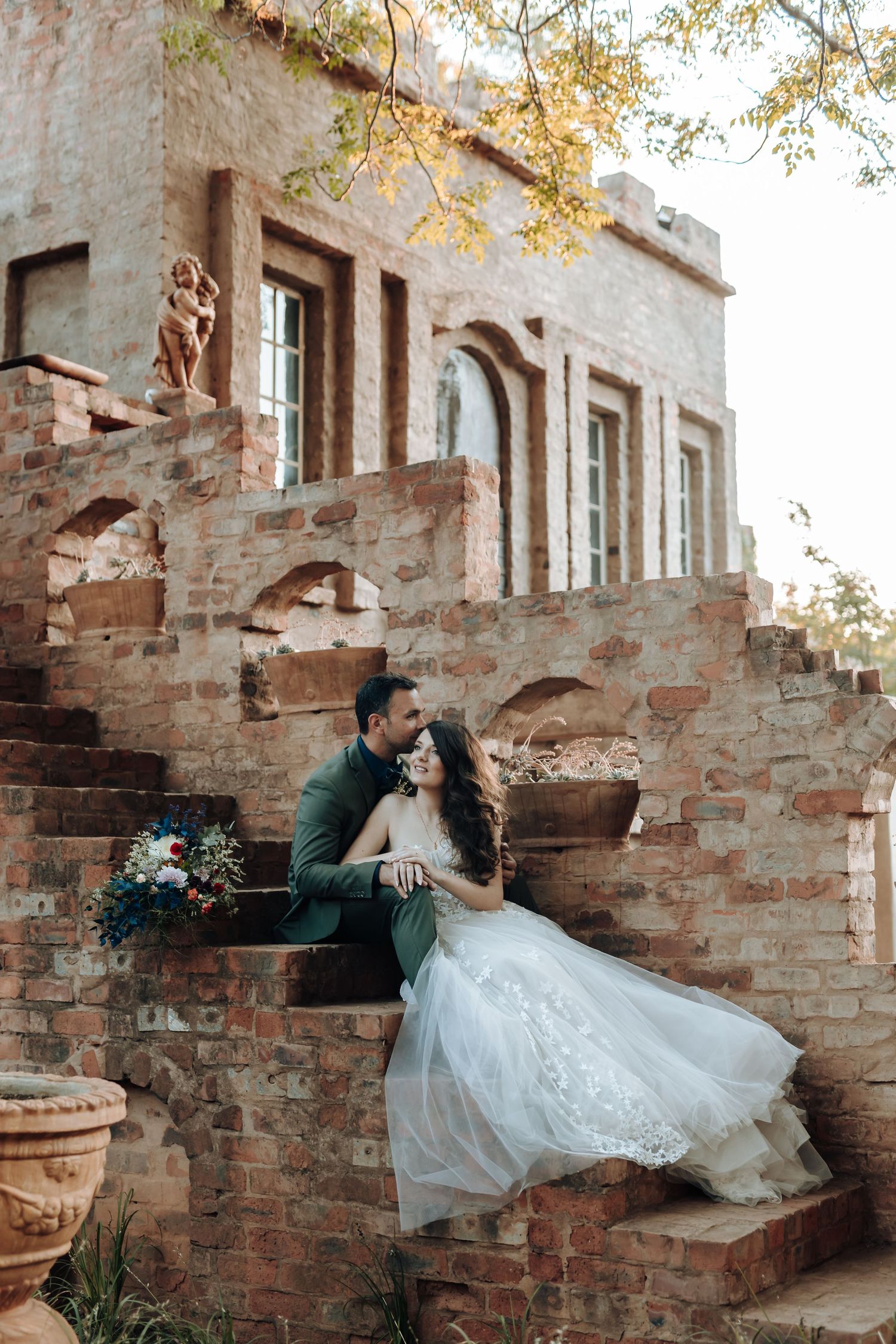 Elegant wedding portrait on stone steps with flowing white dress and architectural backdrop.
