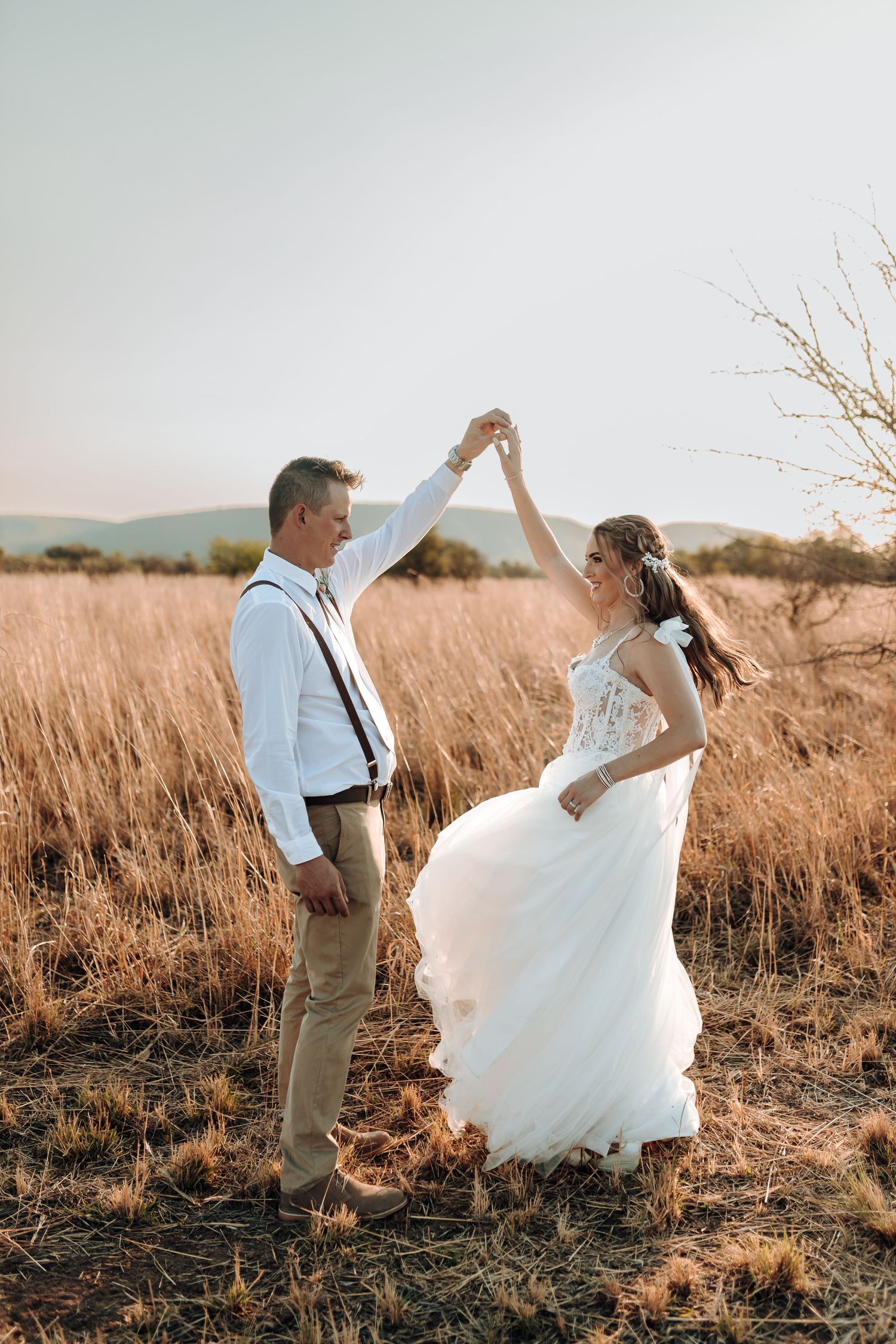 Dancing newlyweds share romantic moment in field of dried grass during golden hour.