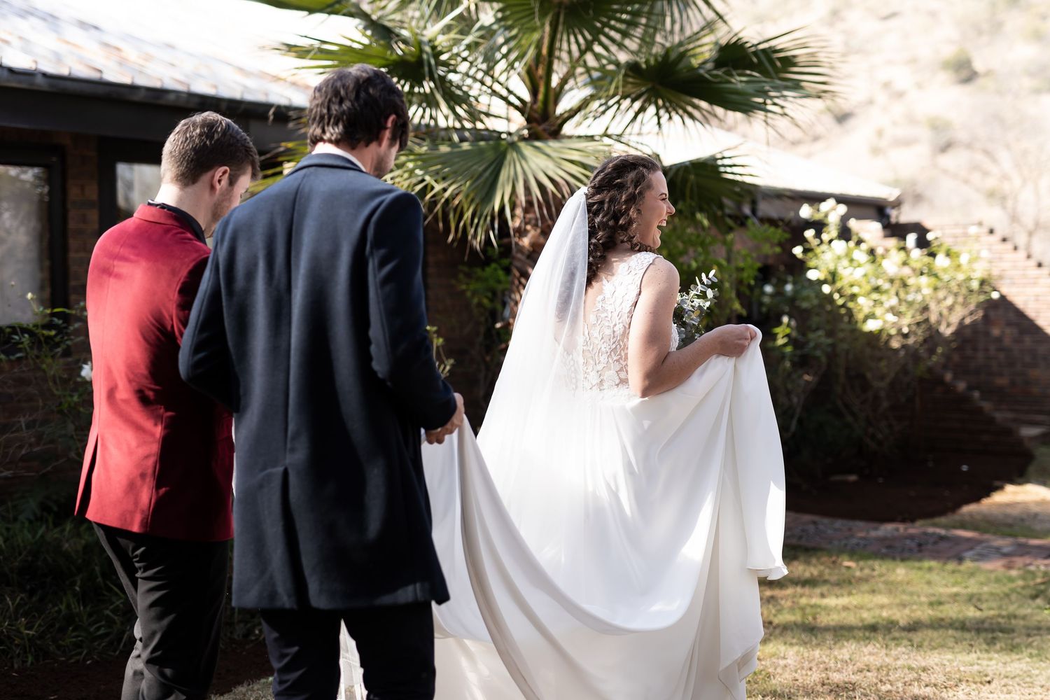 Wedding ceremony scene captured in outdoor garden setting with bride's flowing white dress visible against natural backdrop.