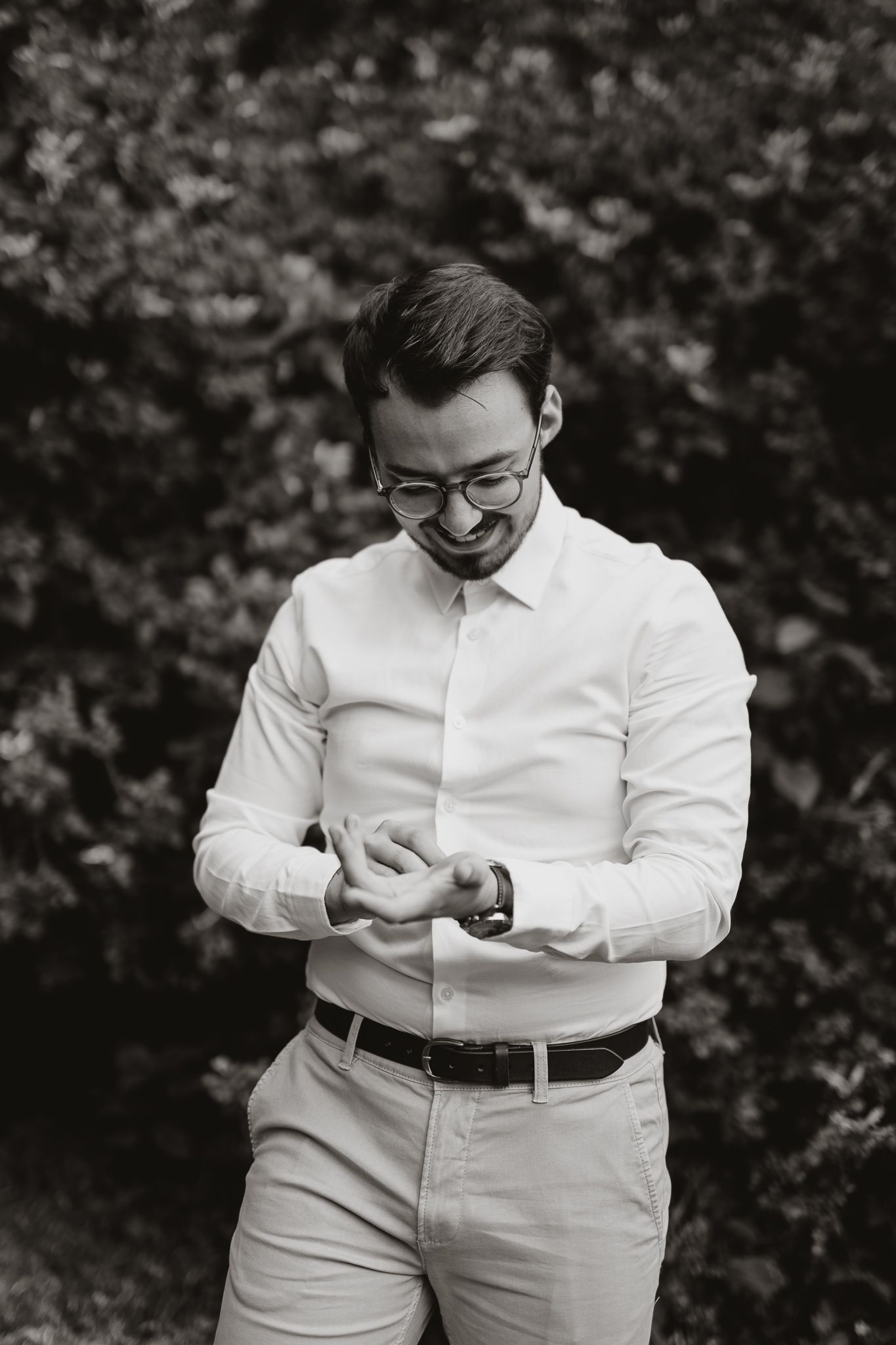 Groom in white dress shirt and glasses smiling while adjusting cuffs.