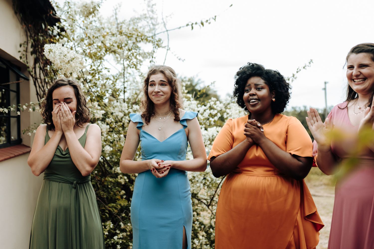 Bridesmaids in colorful dresses showing surprised reactions during wedding photoshoot.