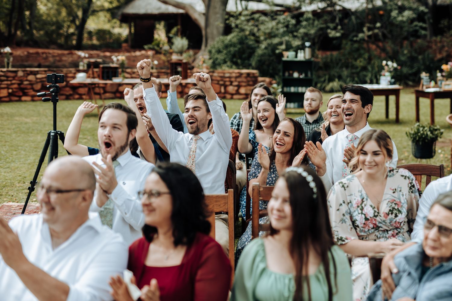 Wedding guests cheer and celebrate with enthusiasm during an outdoor ceremony.