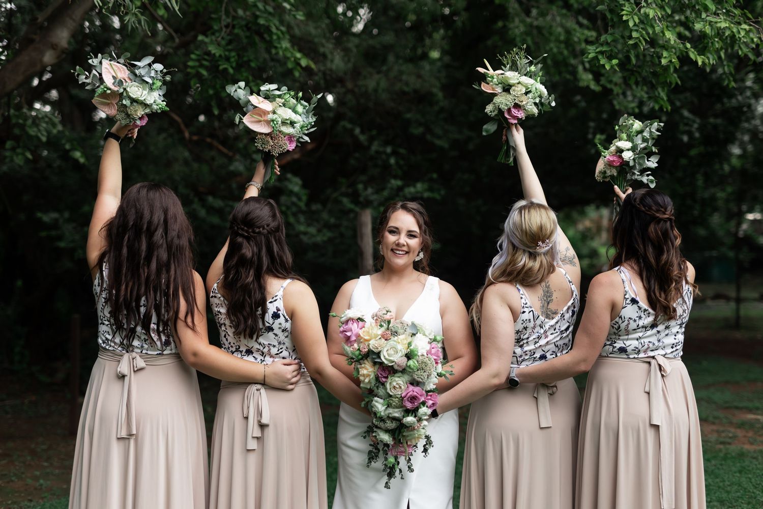 Wedding party poses creatively with bouquets raised in an outdoor garden setting.