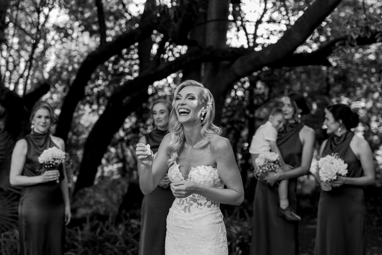 Black and white photo of wedding party laughing during outdoor ceremony.