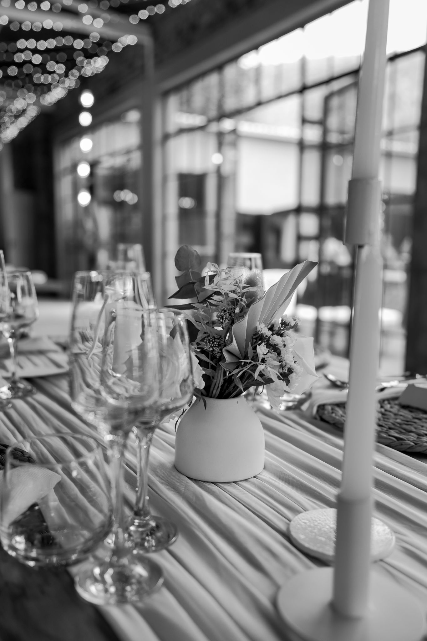 Black and white photo of an elegant table setting with white vase centerpiece and wine glasses.