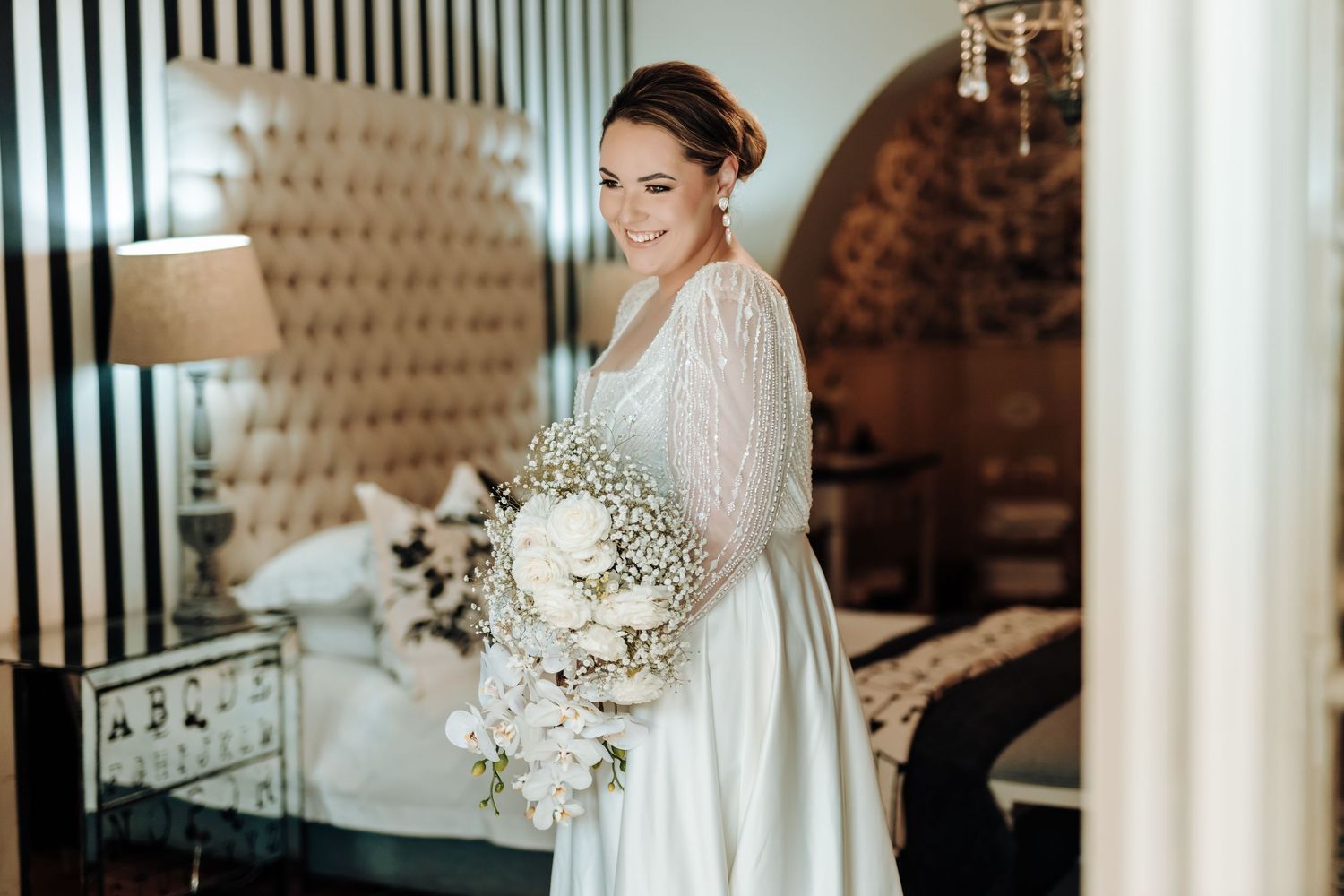 Elegant bridal portrait with a white floral bouquet and long-sleeved beaded wedding gown.