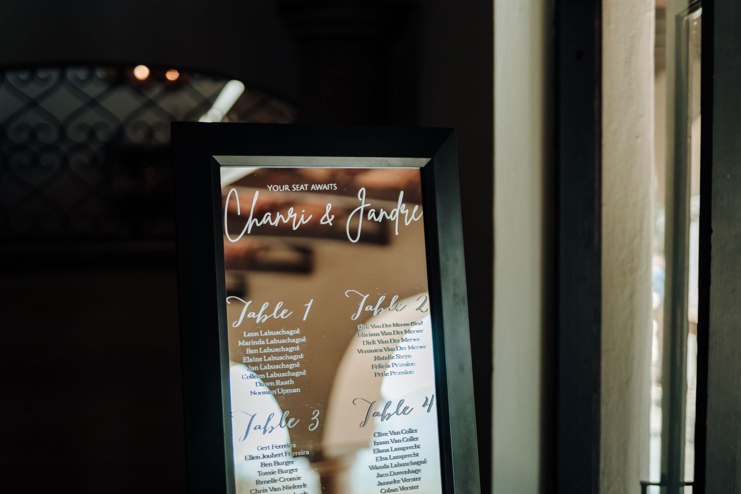Wedding seating chart displayed on reflective surface with elegant script typography.