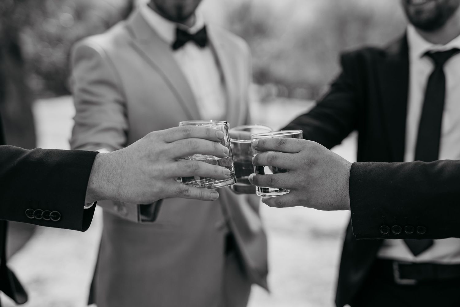Black and white shot of groomsmen toasting with small glasses during wedding celebration.