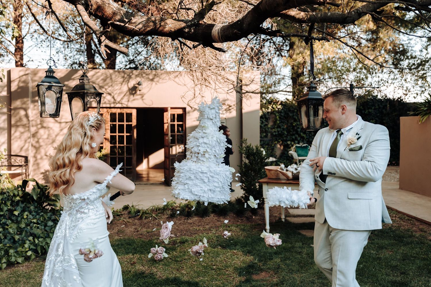 An outdoor wedding reception scene with a white tiered cake and elegant garden decor.