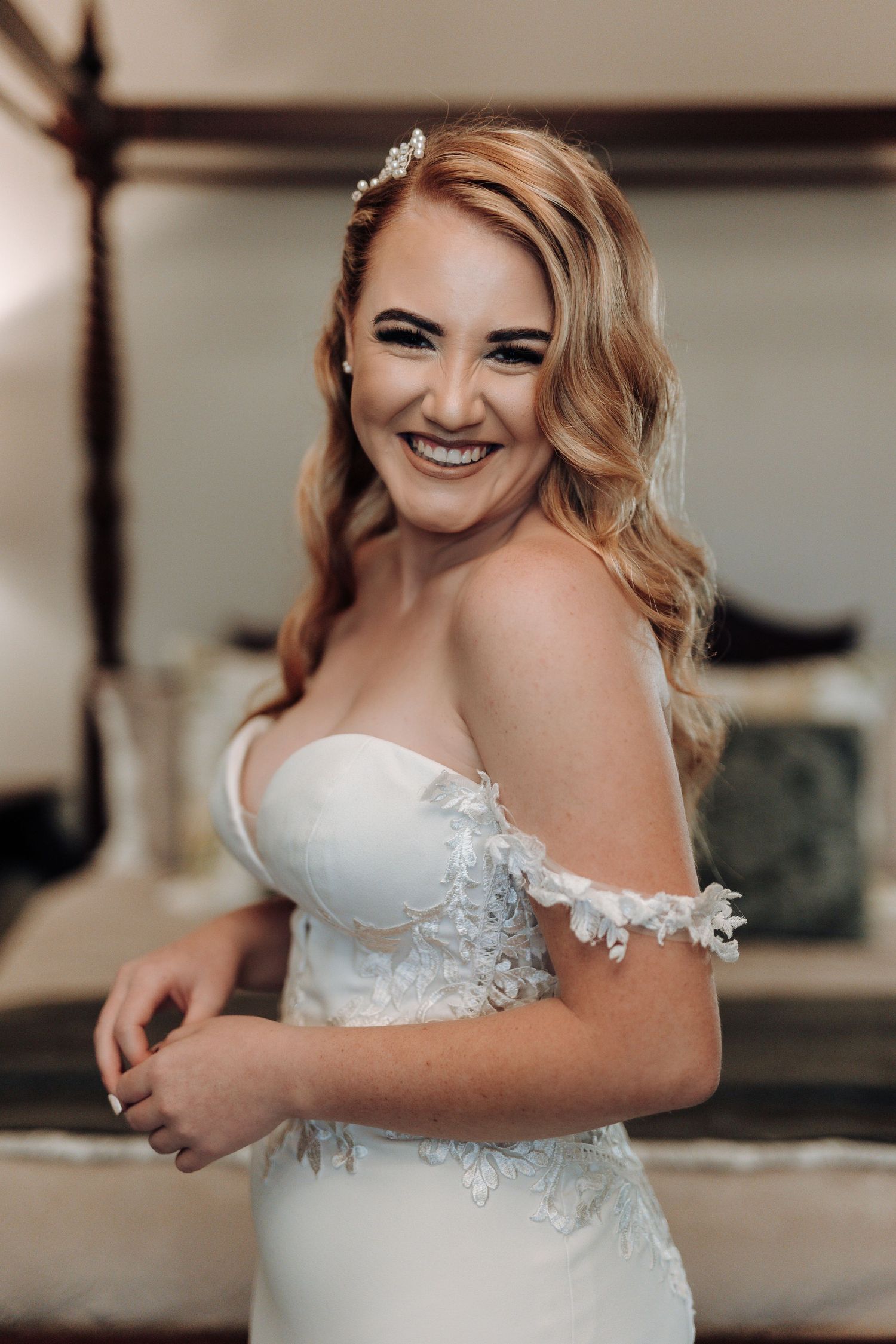 Radiant bride laughing with styled blonde hair wearing strapless lace wedding gown.