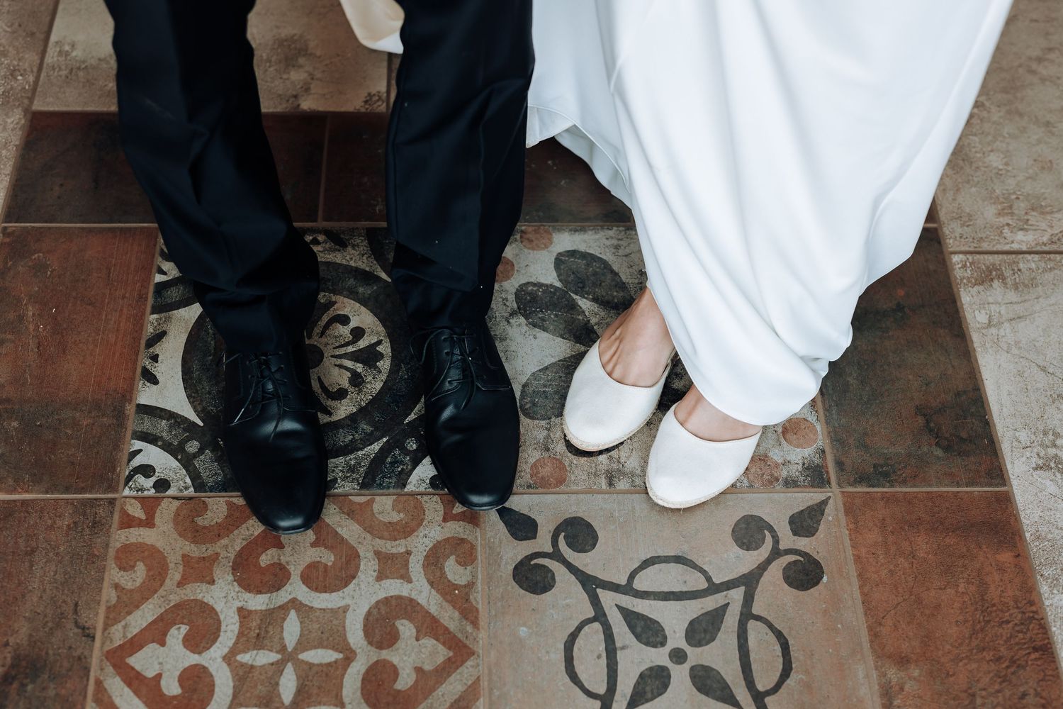 Wedding couple's feet showing traditional dress shoes on decorative tiled floor.