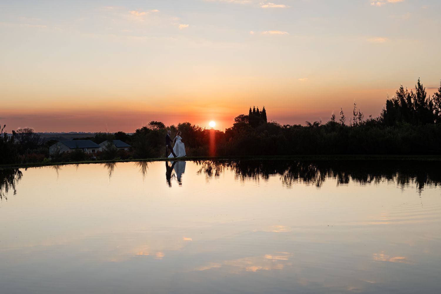 Silhouettes of a couple reflected in still water at sunset.