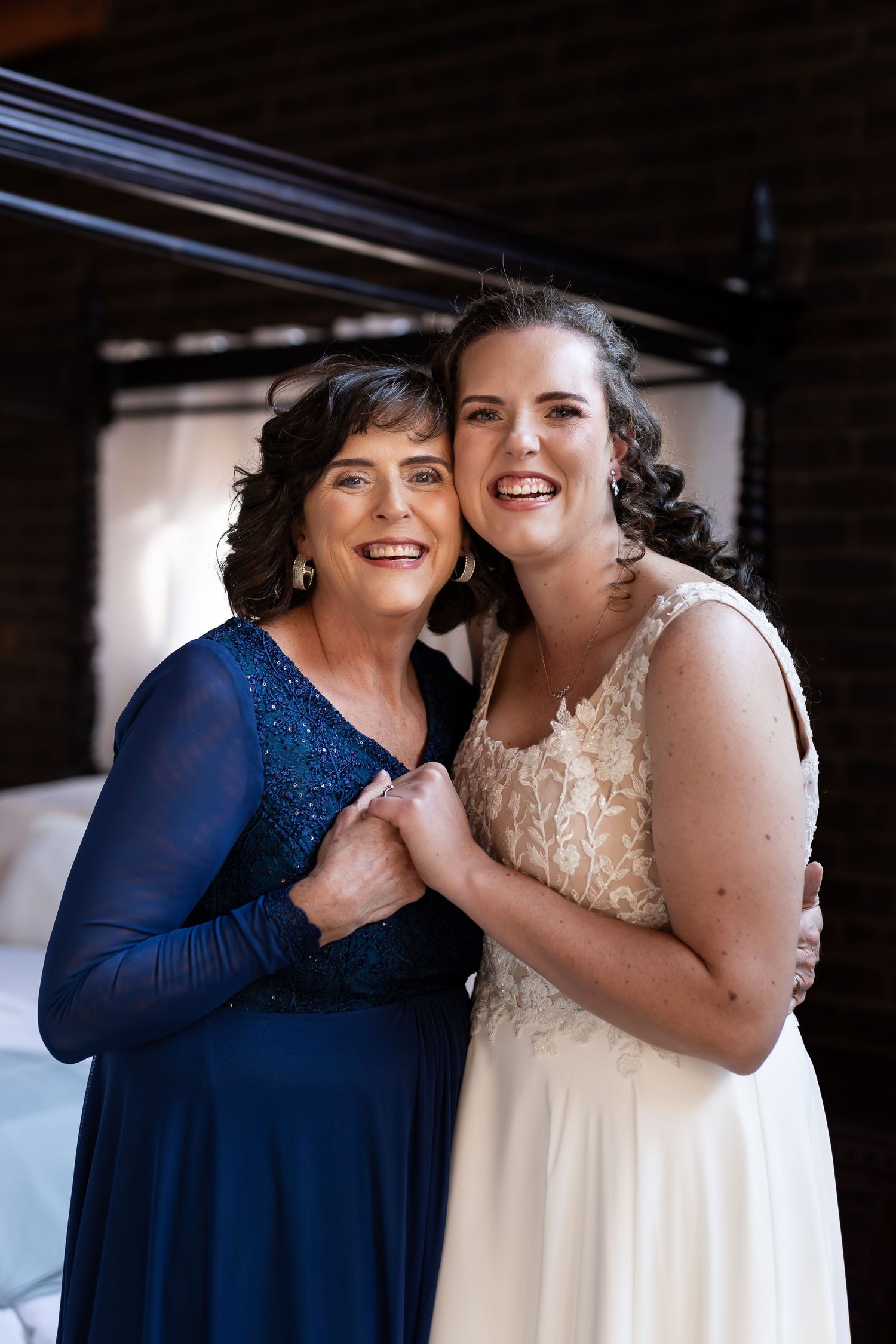 Two women share a joyful moment together, one wearing a navy blue dress and one in a white wedding gown.
