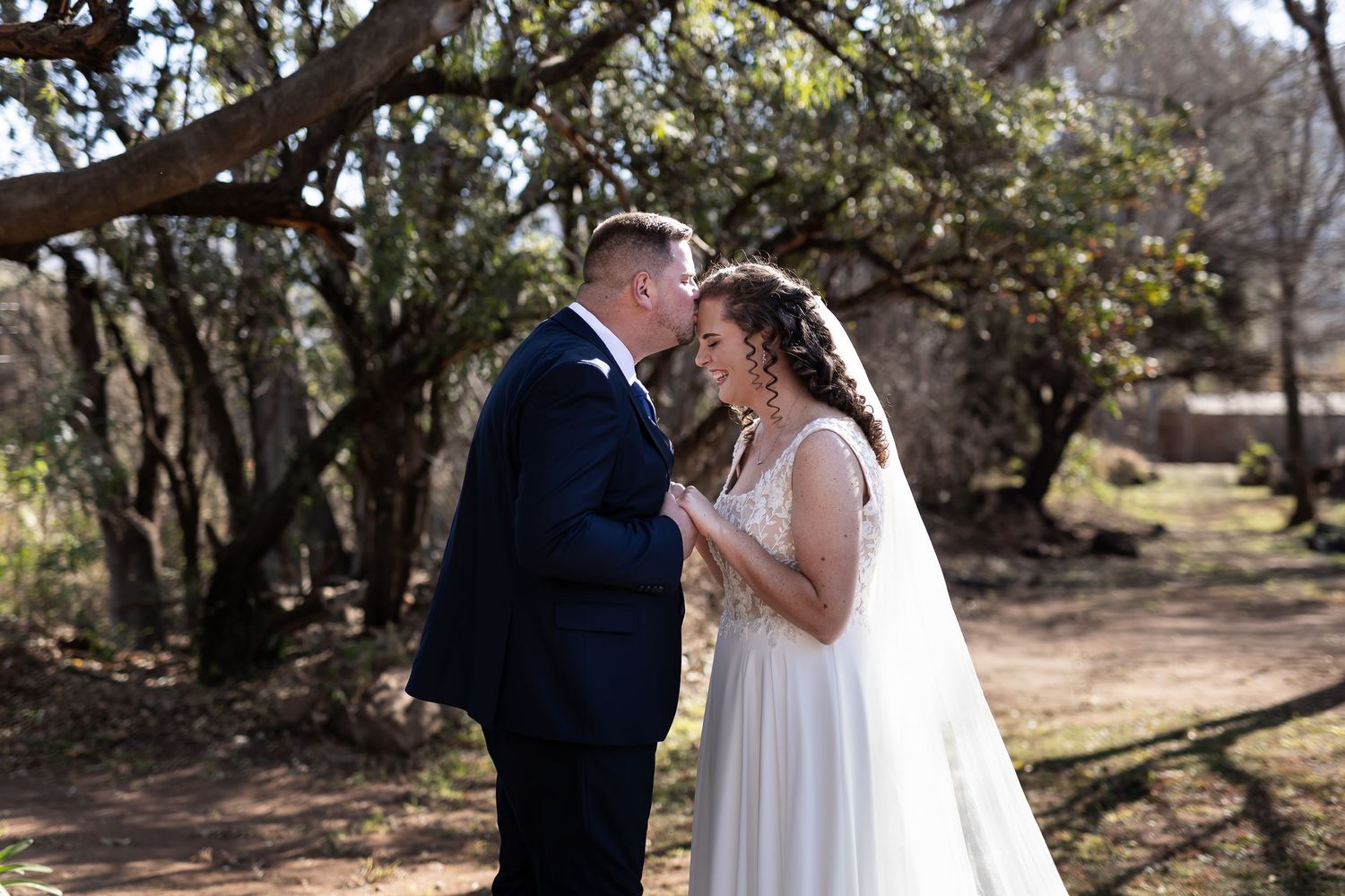 A couple in wedding attire embraces while standing in a scenic outdoor garden setting during their special day.