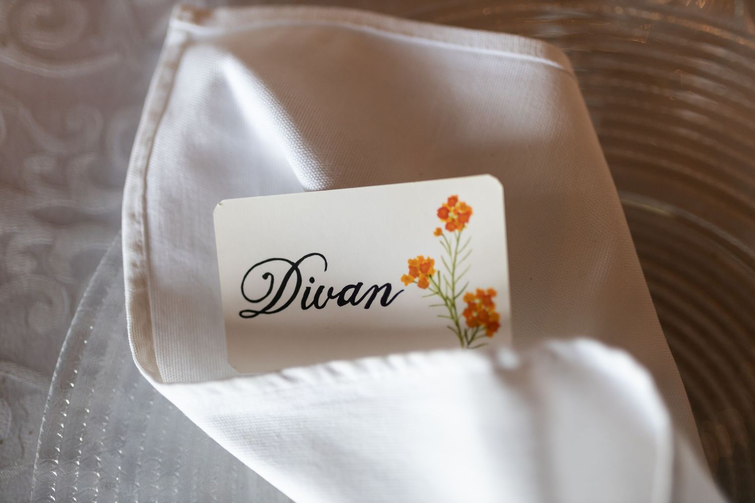 Wedding place card with elegant script reading 'Divan' on white napkin.